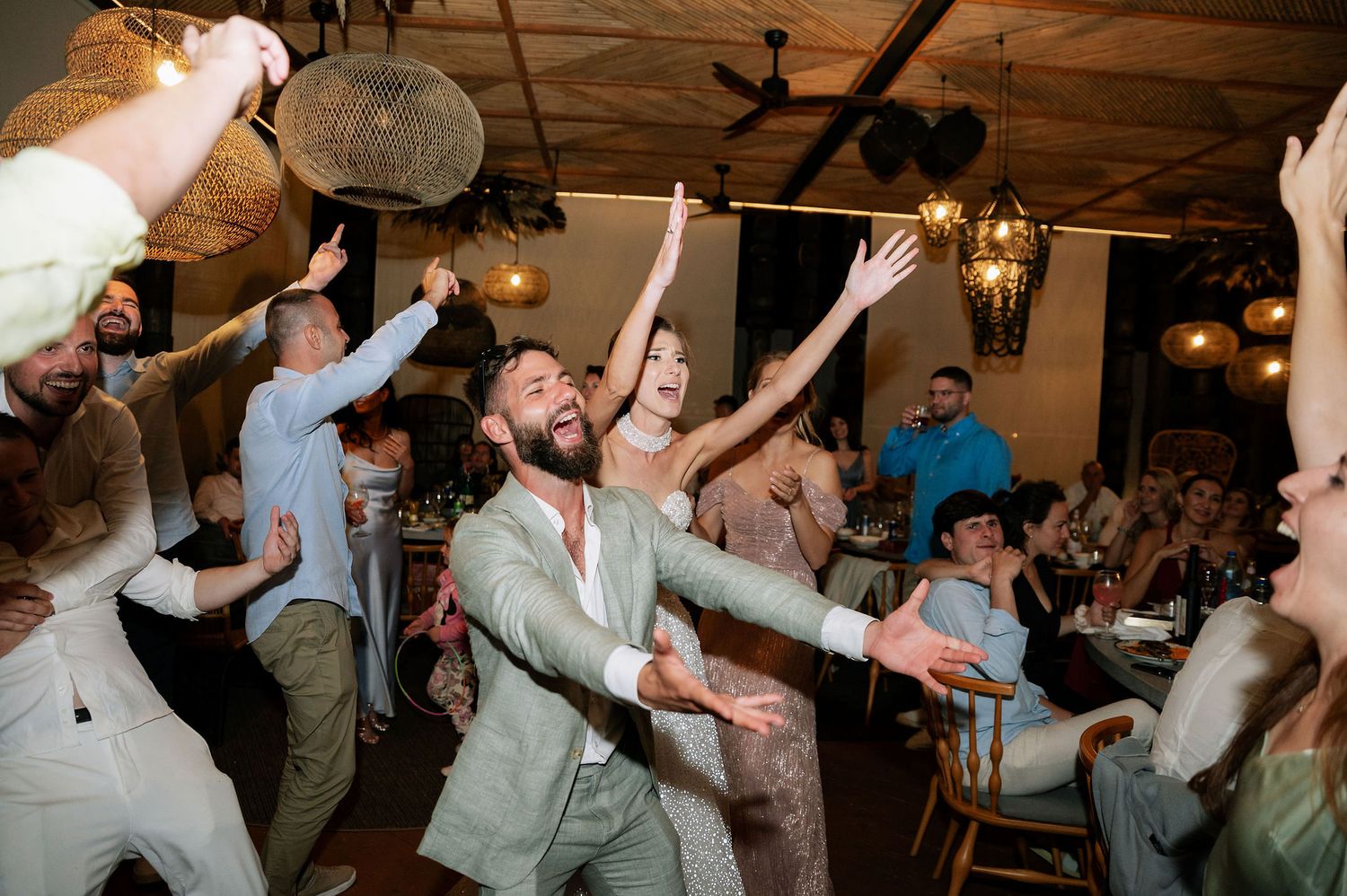 Wedding reception guests dancing enthusiastically with arms raised on a lively dance floor.