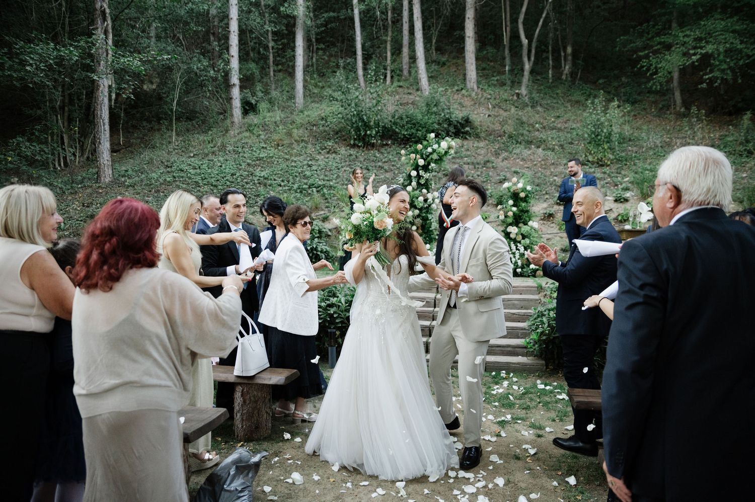 Wedding celebration unfolds in a natural woodland setting with decorative white floral arrangements.