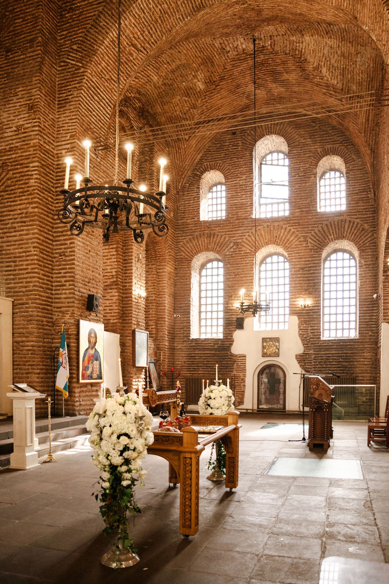 Interior of historic brick church with arched windows, chandeliers, and elegant wedding decor.