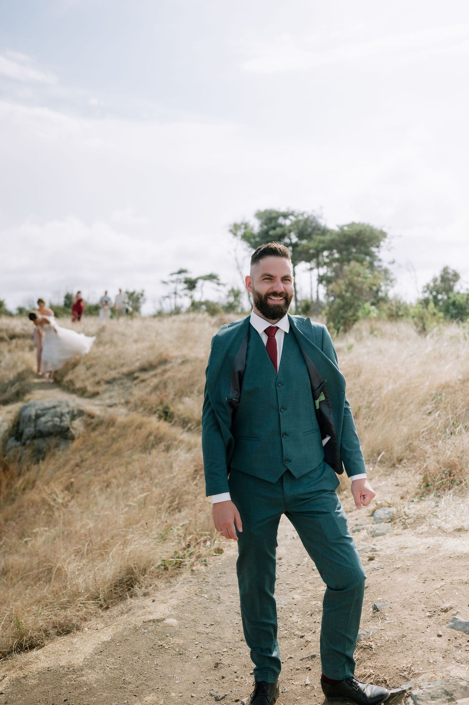 A person in a dark green suit walking along a grassy hilltop path.