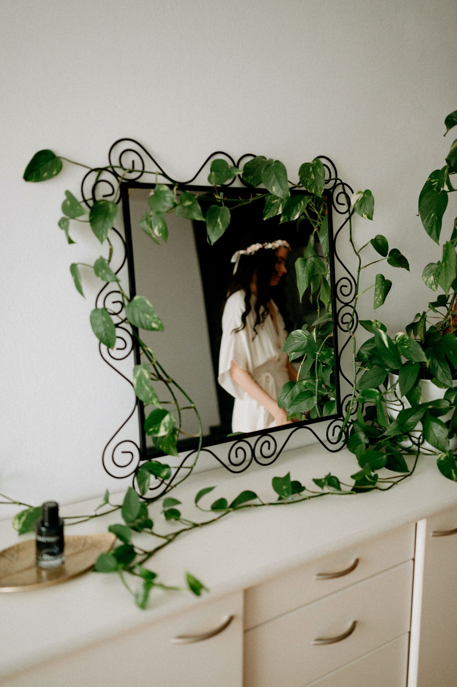 White dresser with decorative mirror and climbing vine plants creating an elegant indoor setting.