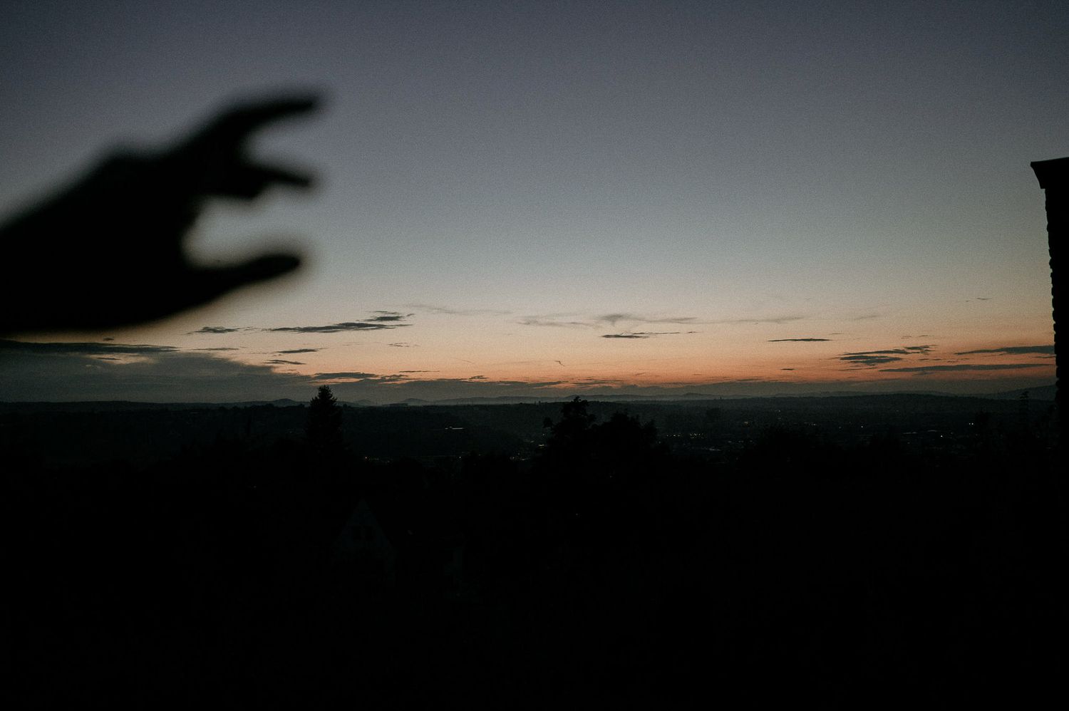 Dramatic sunset sky with dark silhouettes of buildings on the horizon.
