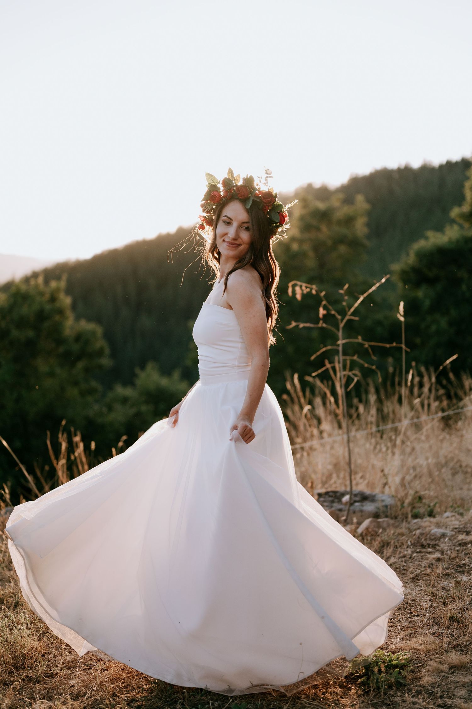 A flowing white wedding dress twirls gracefully against a golden sunset in a mountain field.