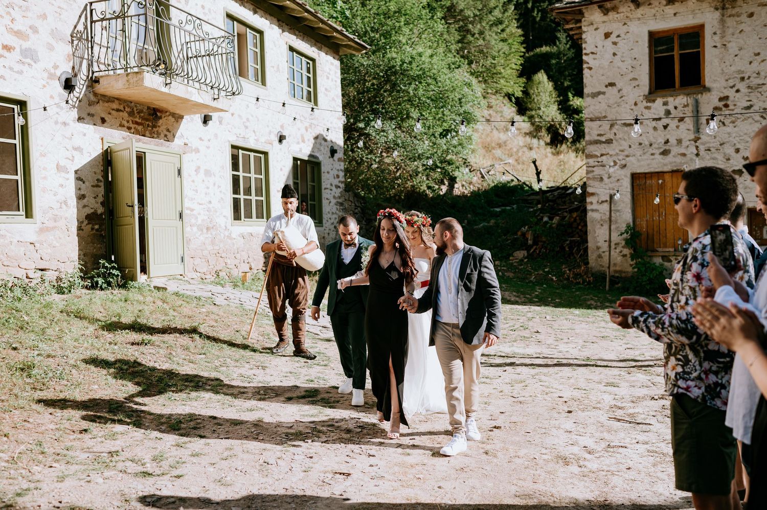 Wedding party and guests gather in courtyard of rustic stone venue for celebrations.