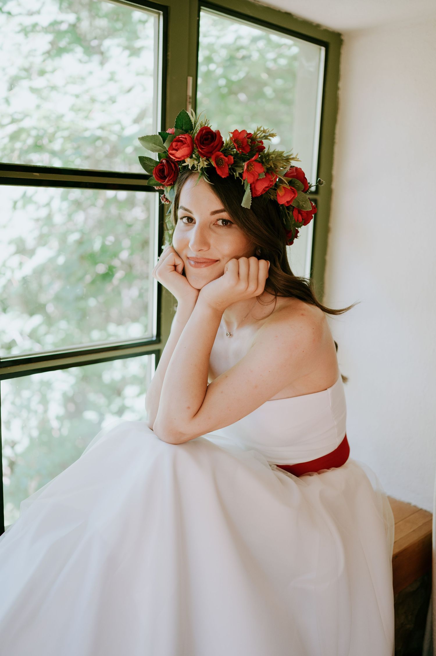 Dreamy bridal portrait with red rose crown and white gown in natural window light.