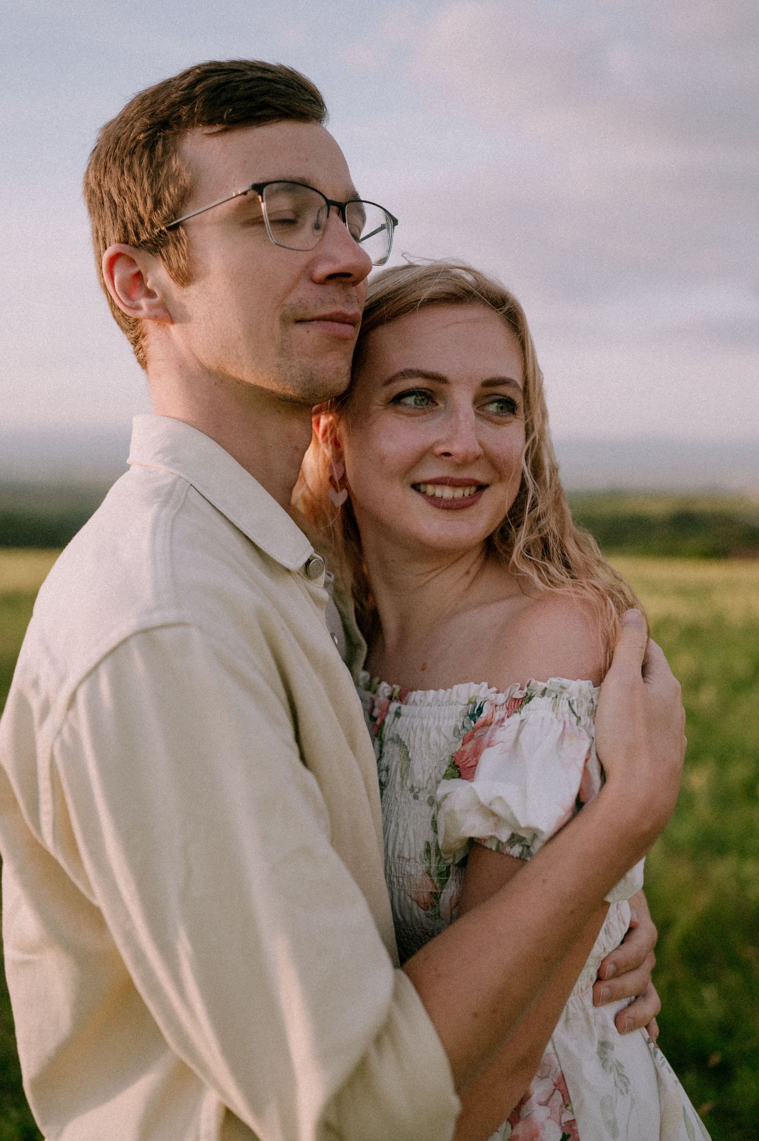 A tender moment between a couple in formal wear standing in a field at sunset.