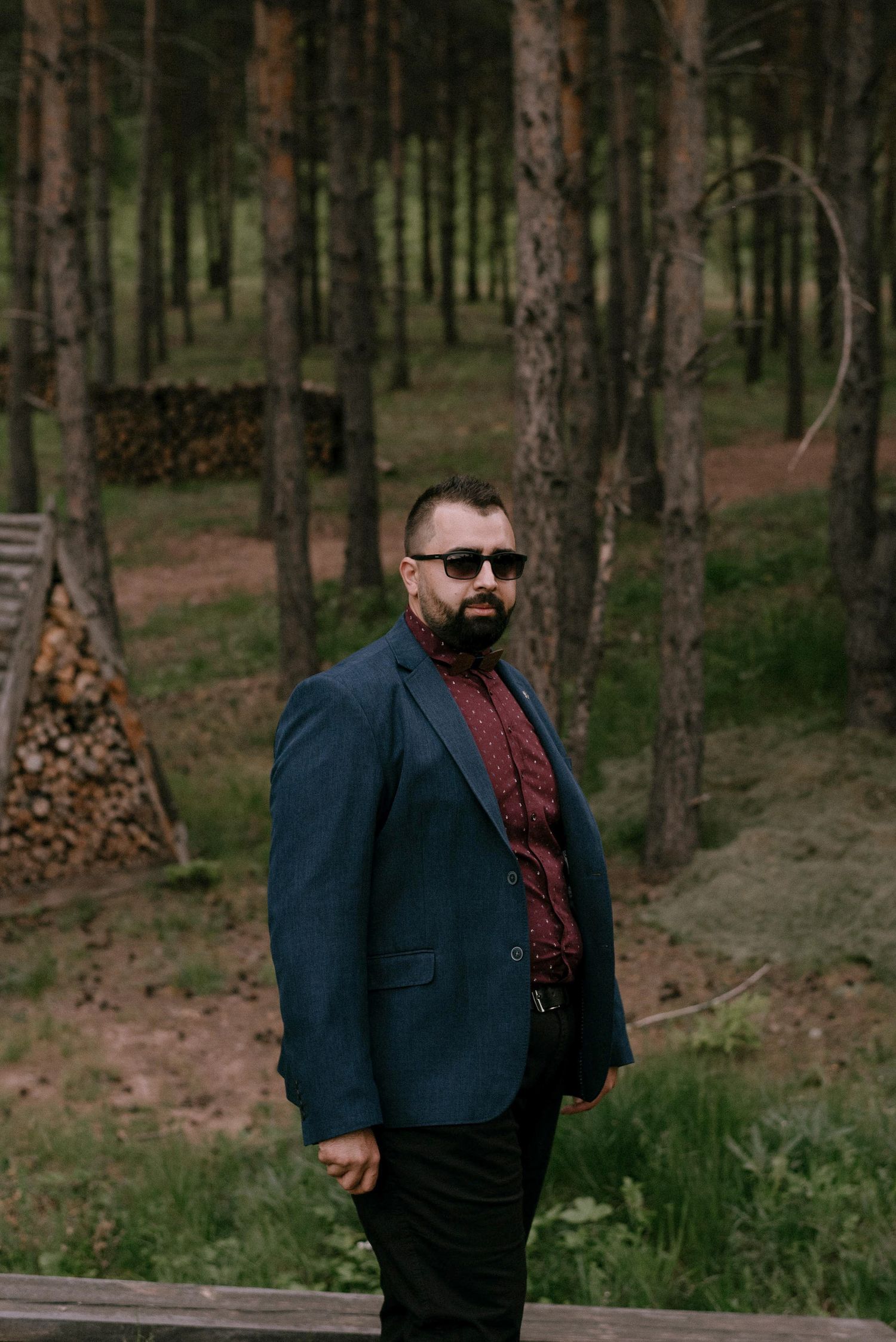 Person in formal attire poses in a wooded forest setting.