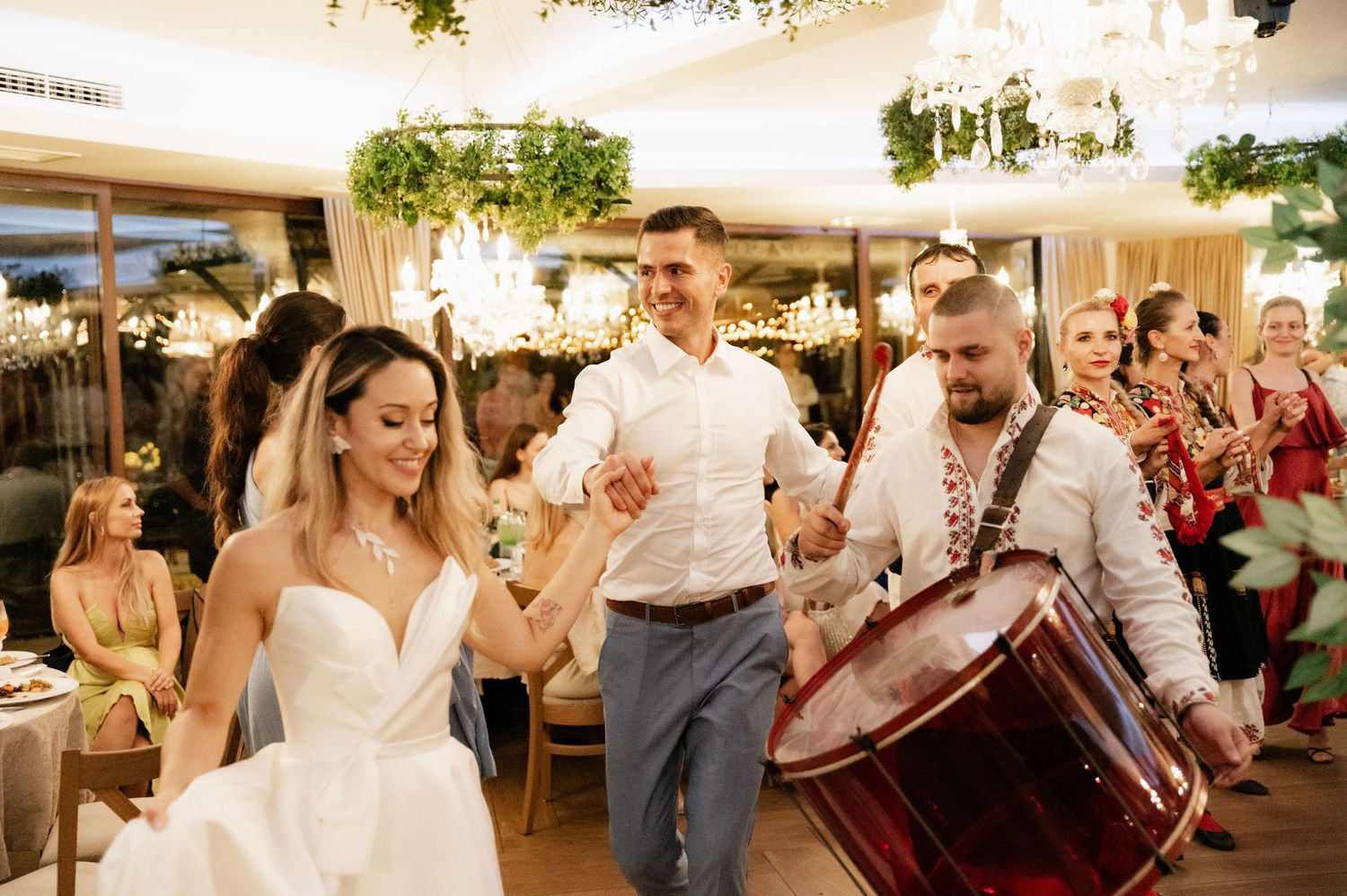 Wedding guests dance and celebrate together during a lively reception party under elegant chandeliers.