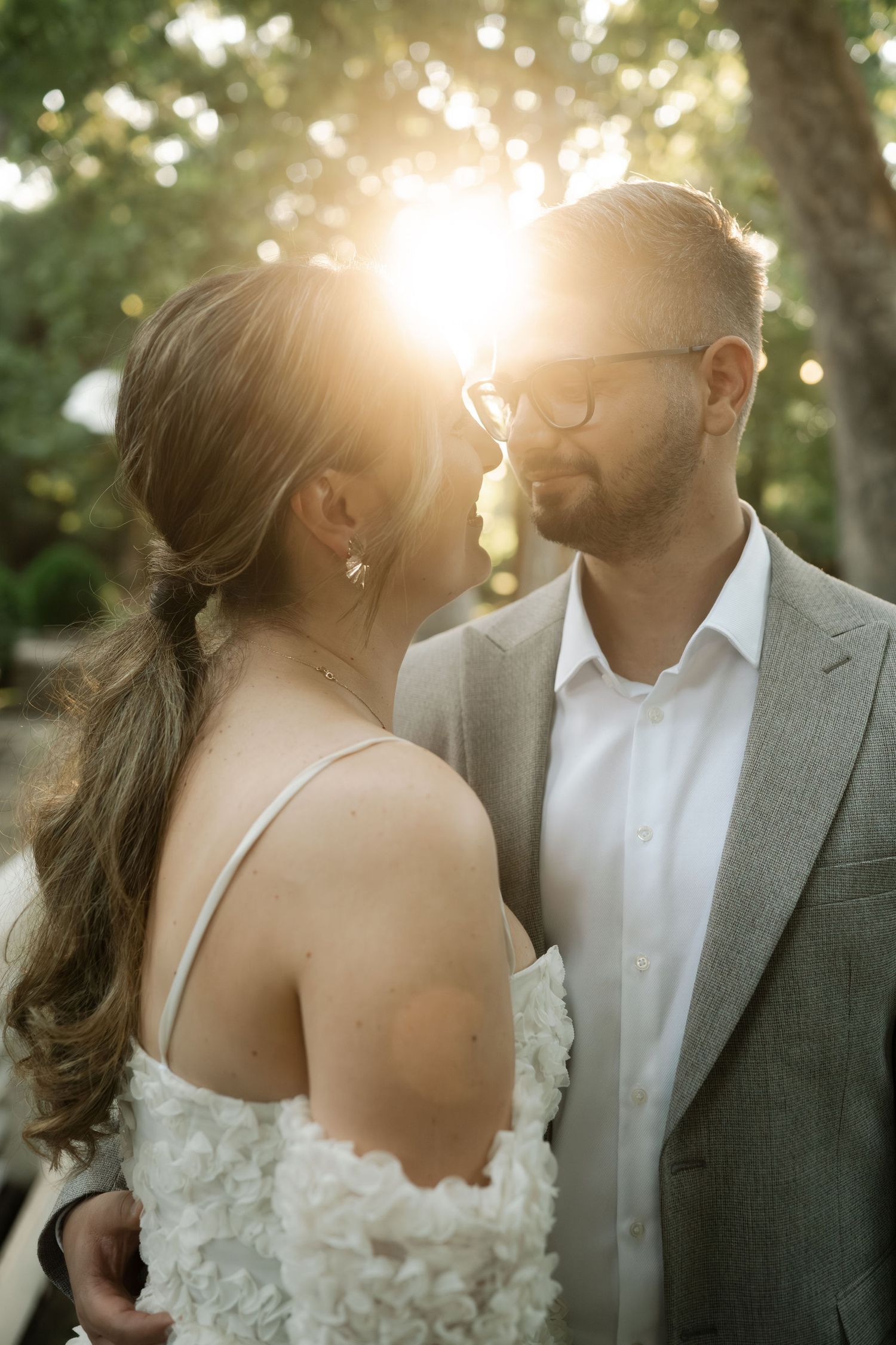 Romantic wedding couple shares intimate moments in a sunlit garden setting with dreamy bokeh lighting effects.