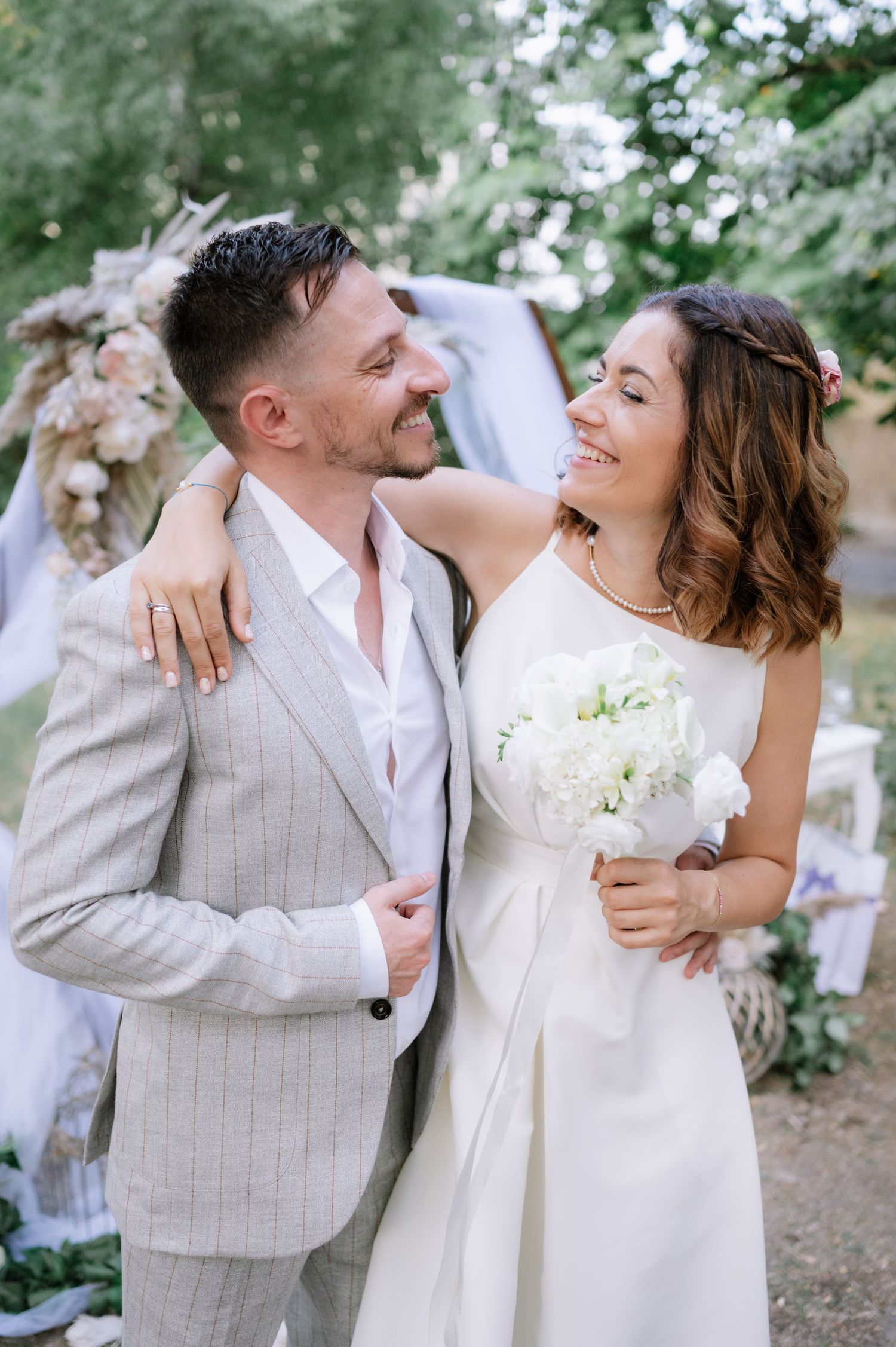 A romantic outdoor wedding photo series showing a couple in light colored attire embracing and laughing joyfully together.