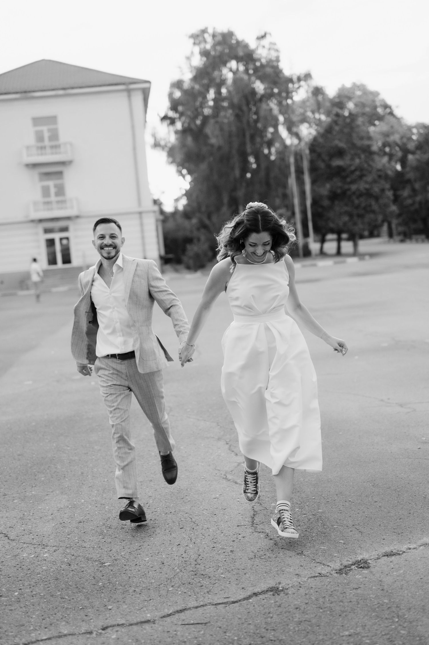 A couple runs playfully across a lawn in black and white wedding attire creating a joyful candid moment.