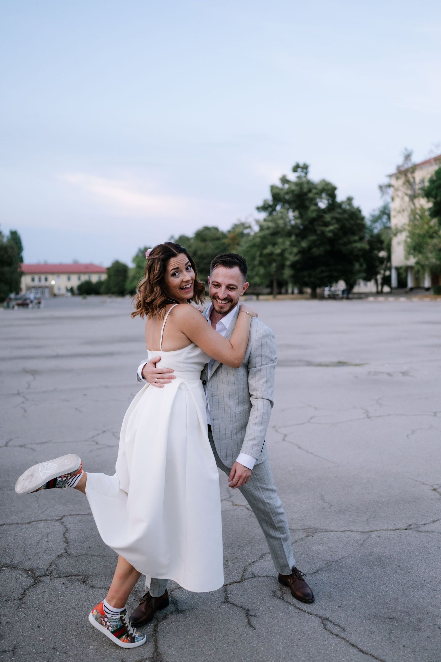 A couple in casual wedding attire playfully dances together on a concrete surface during their photo session.