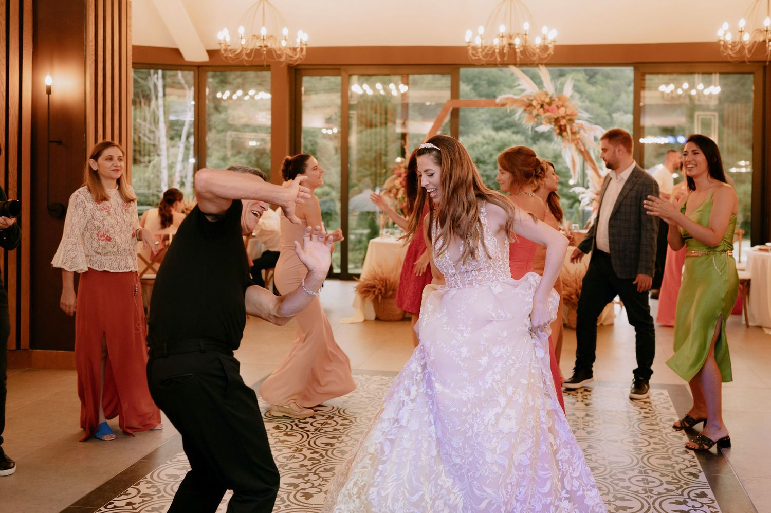 Wedding guests dance together on an elegant ballroom floor under crystal chandeliers during a reception celebration.