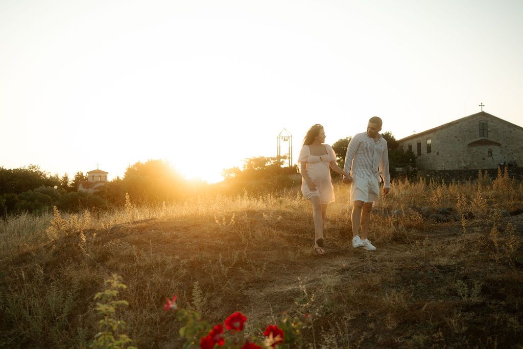 A group of people walk along a grassy hill at sunset creating silhouettes against the golden sky.