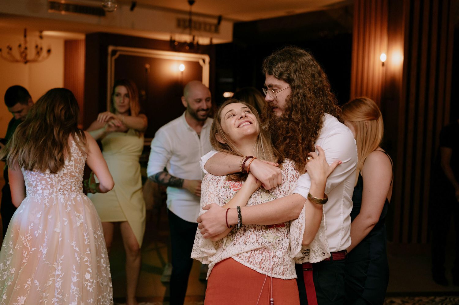 Wedding guests dancing and enjoying themselves at a dimly lit reception venue with warm lighting.