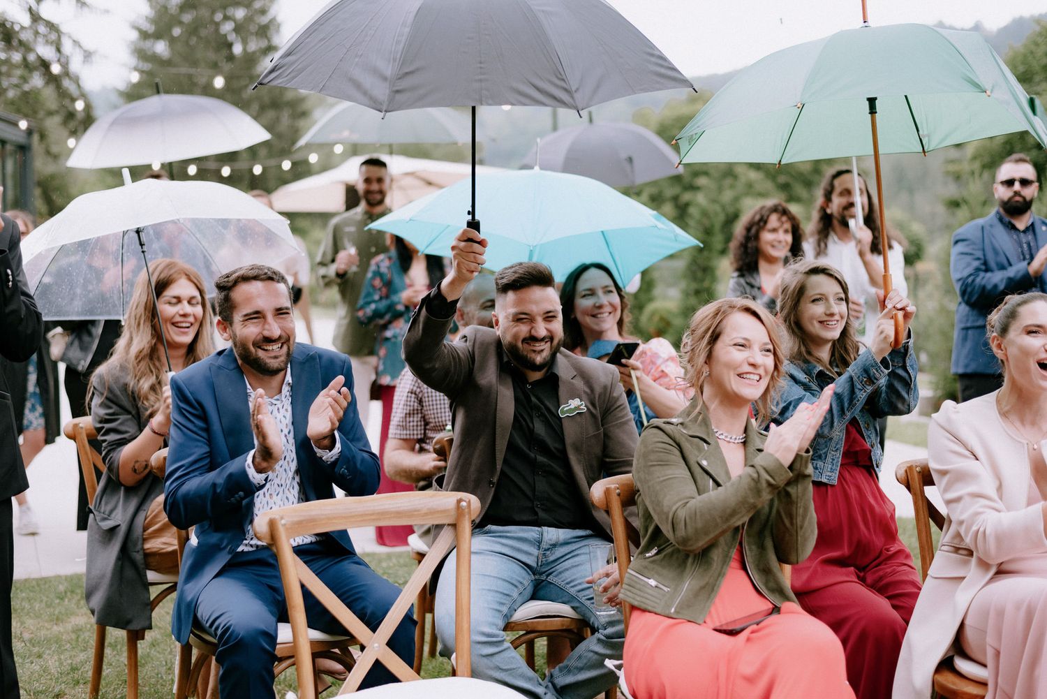Guests gather under umbrellas at an outdoor event on a rainy day, creating a cozy atmosphere despite the weather.