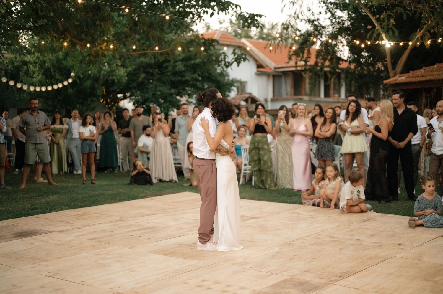 A series of wedding reception photos showing guests dancing and celebrating outdoors under string lights at dusk.
