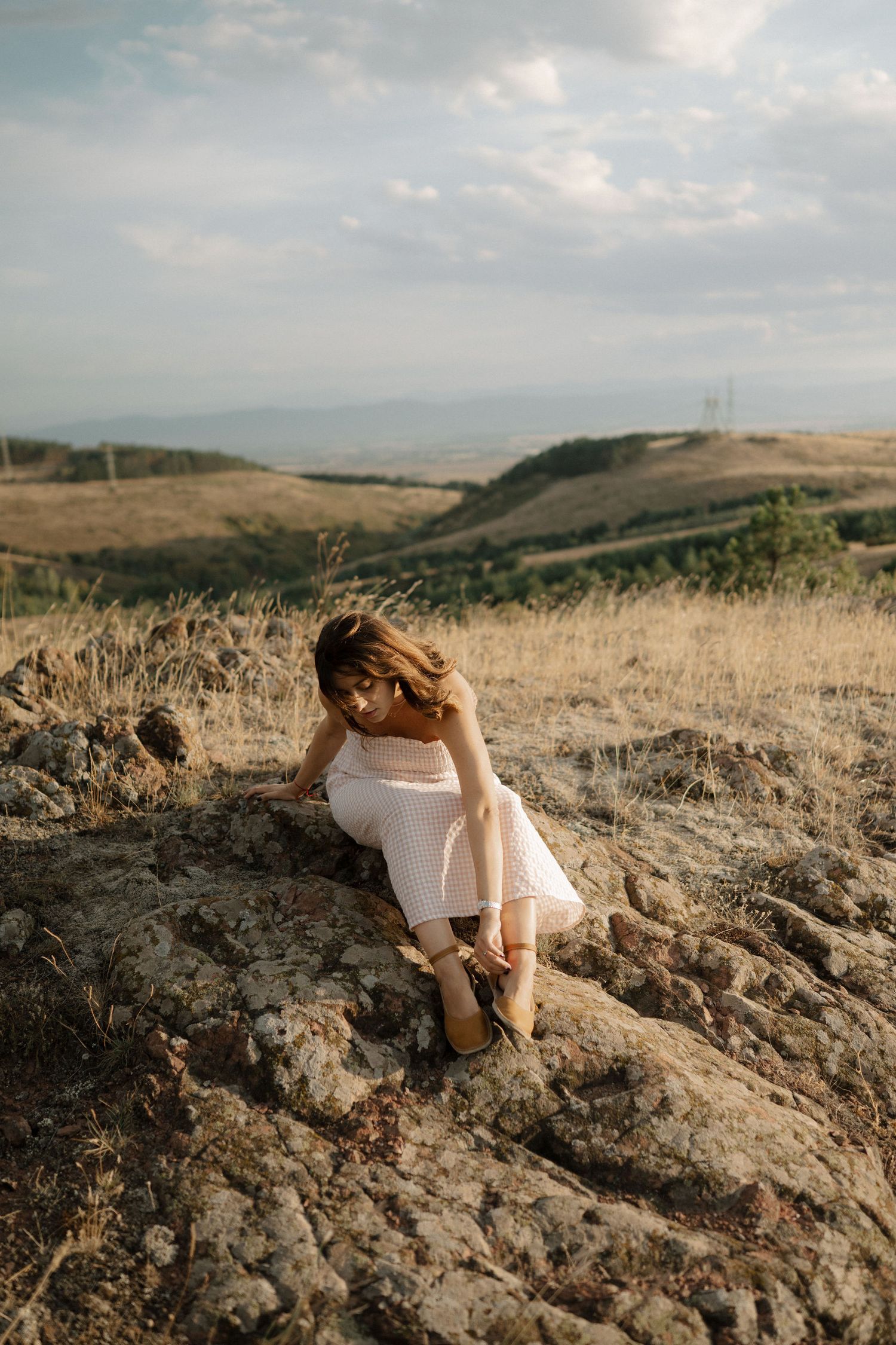 A figure in white sits contemplatively on rocky terrain against a misty mountain landscape at sunset.