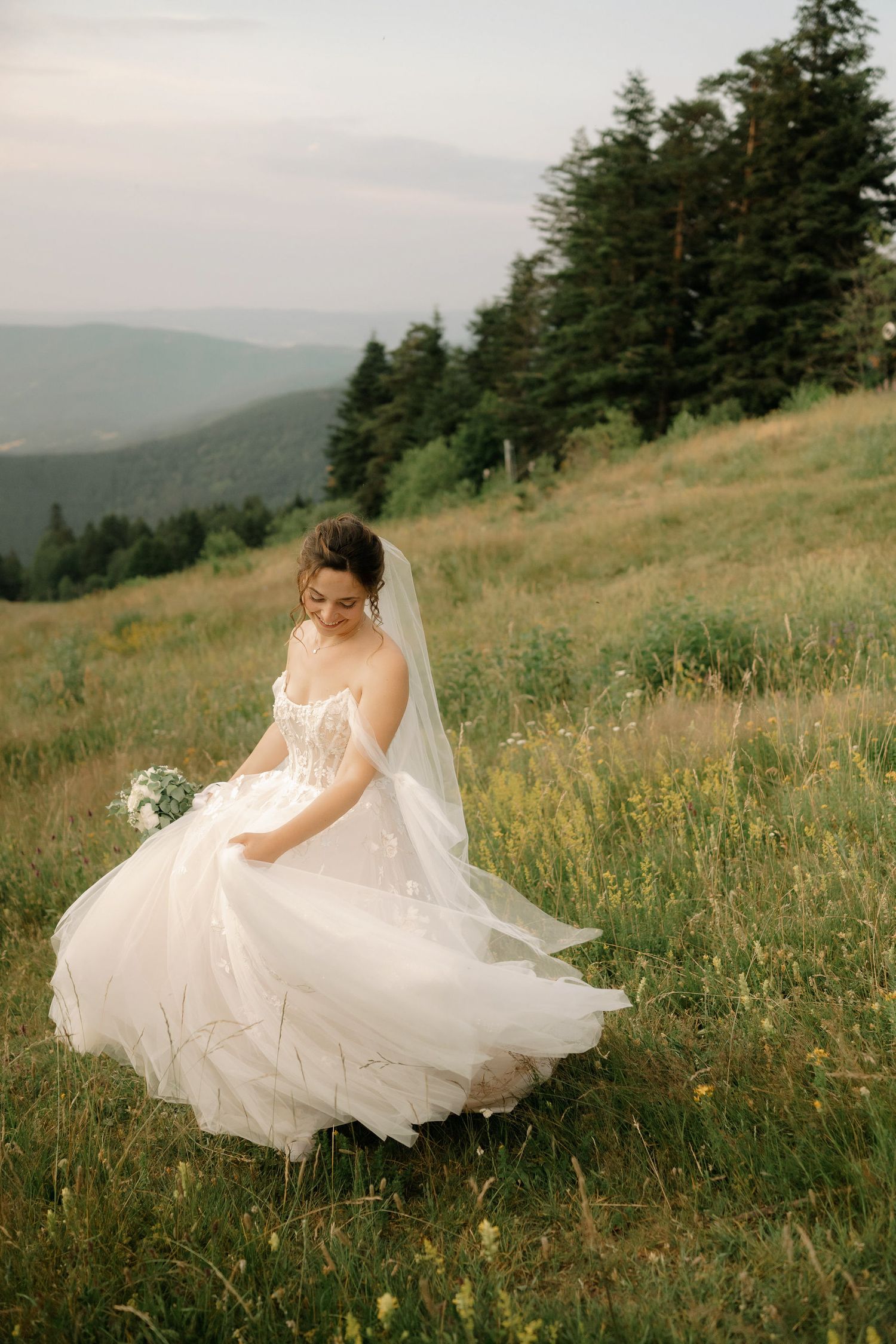A flowing white wedding dress twirls gracefully in a mountain meadow filled with wildflowers at sunset.