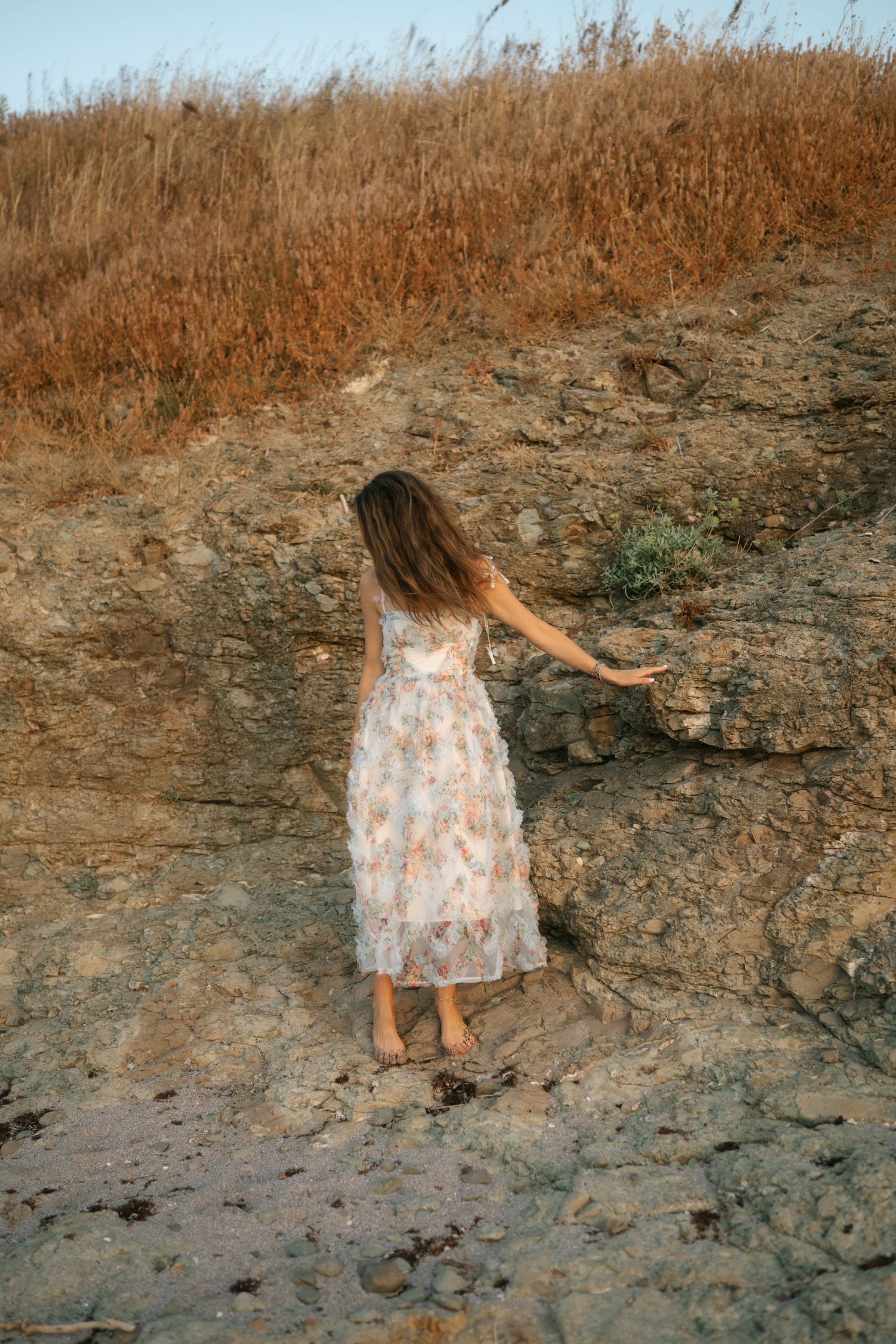 A series of images showing someone in a floral dress climbing up a rocky cliff face near dry grass.