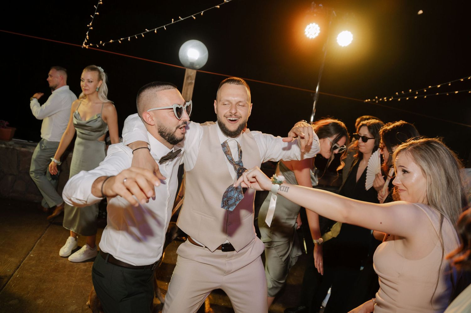 Wedding guests dance and celebrate together on a dimly lit dance floor during an evening reception party.