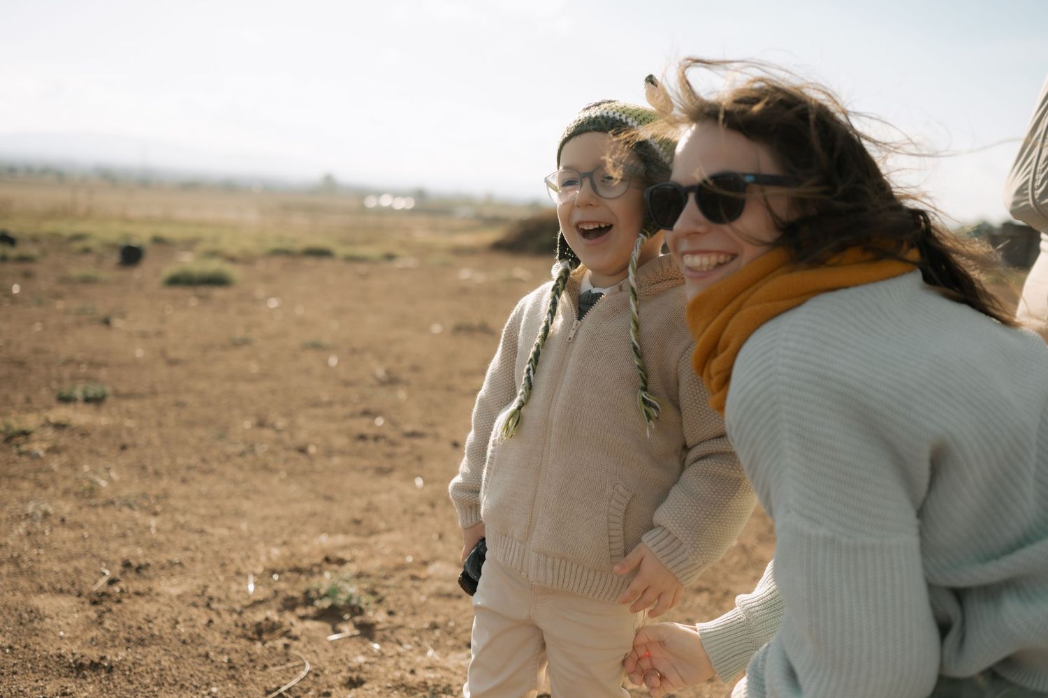 Two people walk together and laugh while exploring a desert landscape on a sunny day.