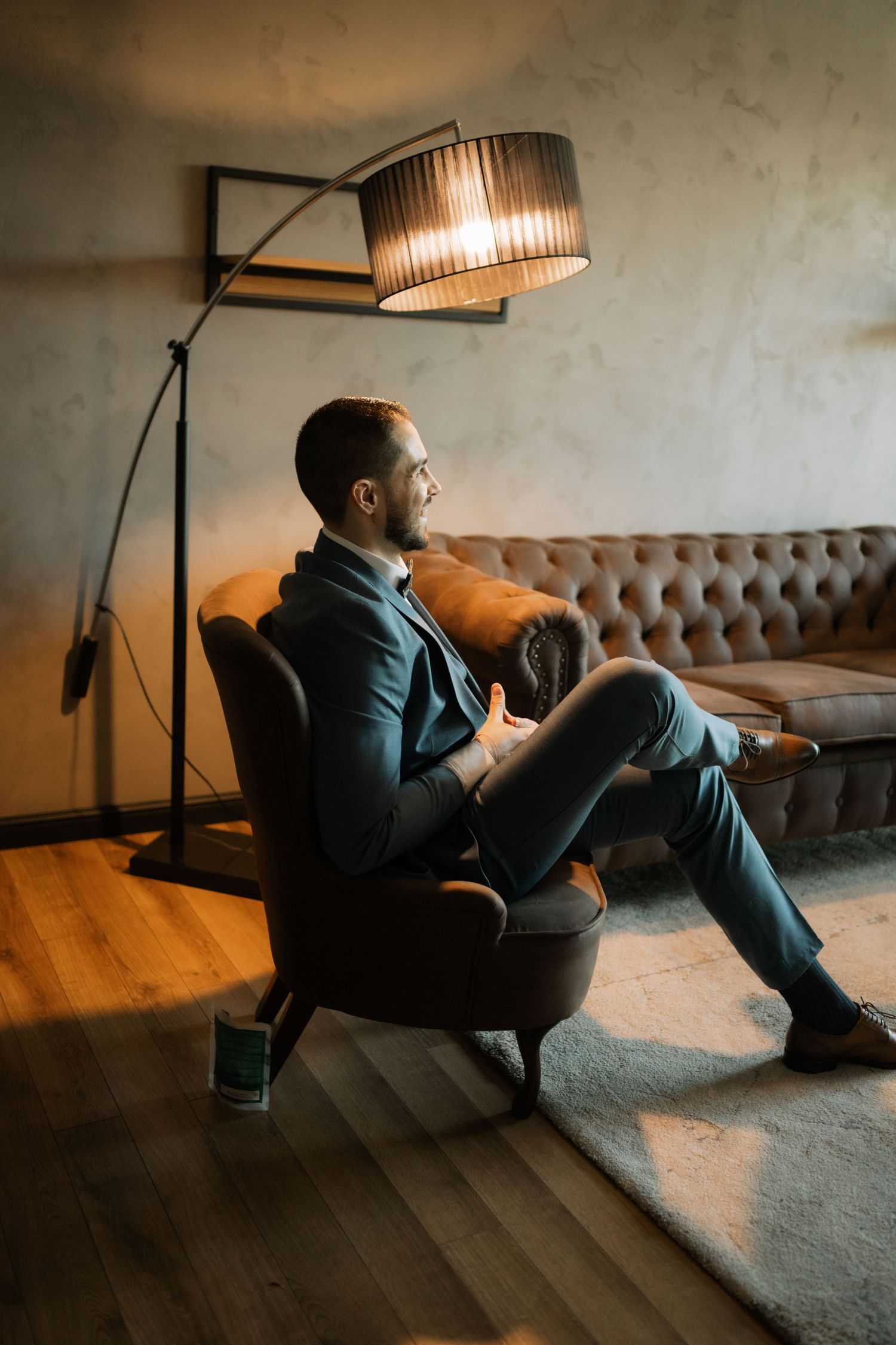Person in dark clothing relaxes on a tufted sofa in a dimly lit room with modern lighting fixtures.