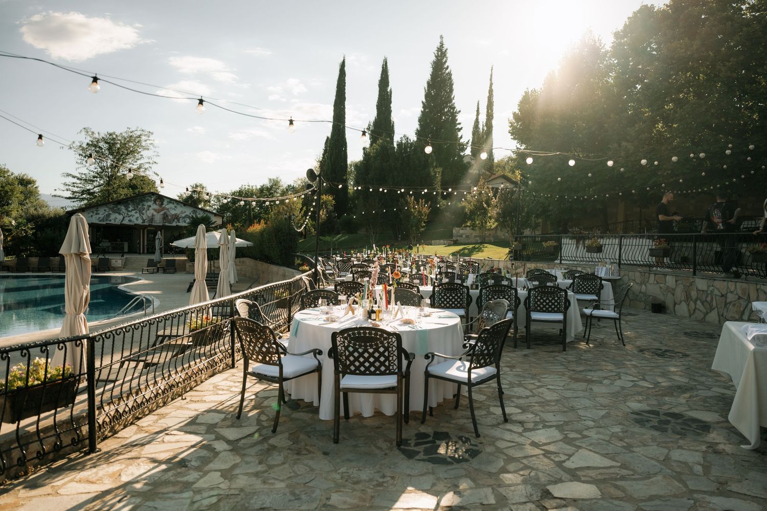 Outdoor wedding reception venue with rustic wooden tables and chairs set against a scenic mountain landscape at sunset.