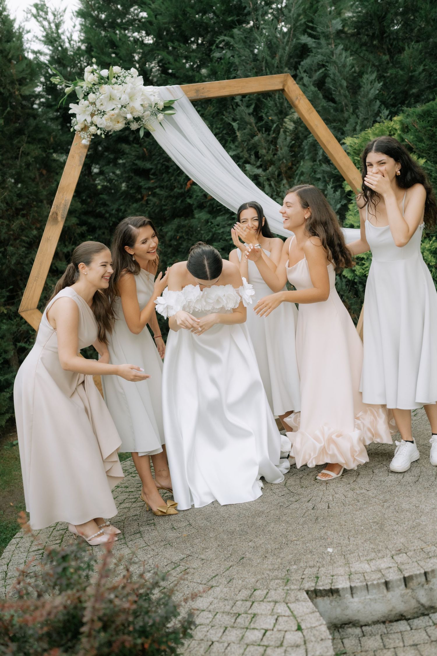 A group in white dresses and light colored attire pose playfully together in a series of candid shots outdoors.