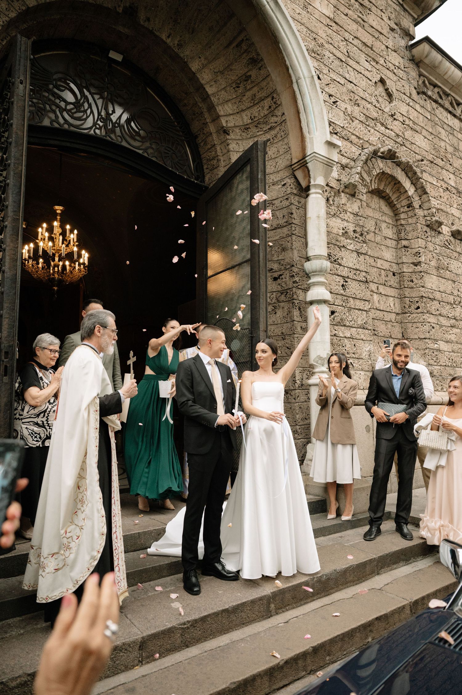 Wedding party gathers under stone archways of historic building during celebration.