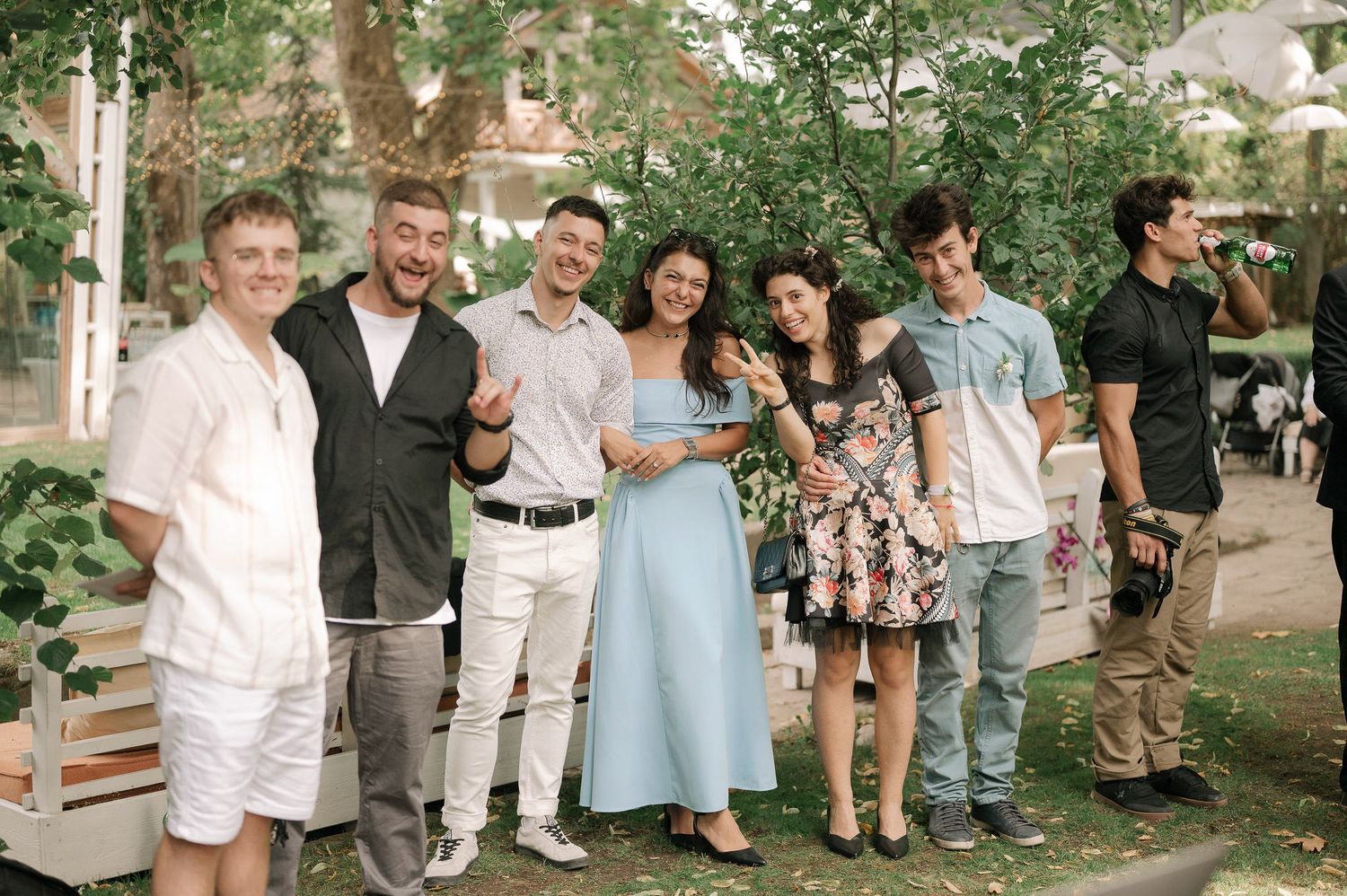 A group of wedding guests gathered outdoors in a garden setting for candid photos.