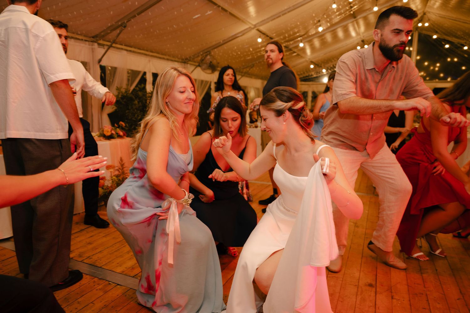 Wedding guests dance and celebrate together on a warmly lit wooden dance floor during a reception party.