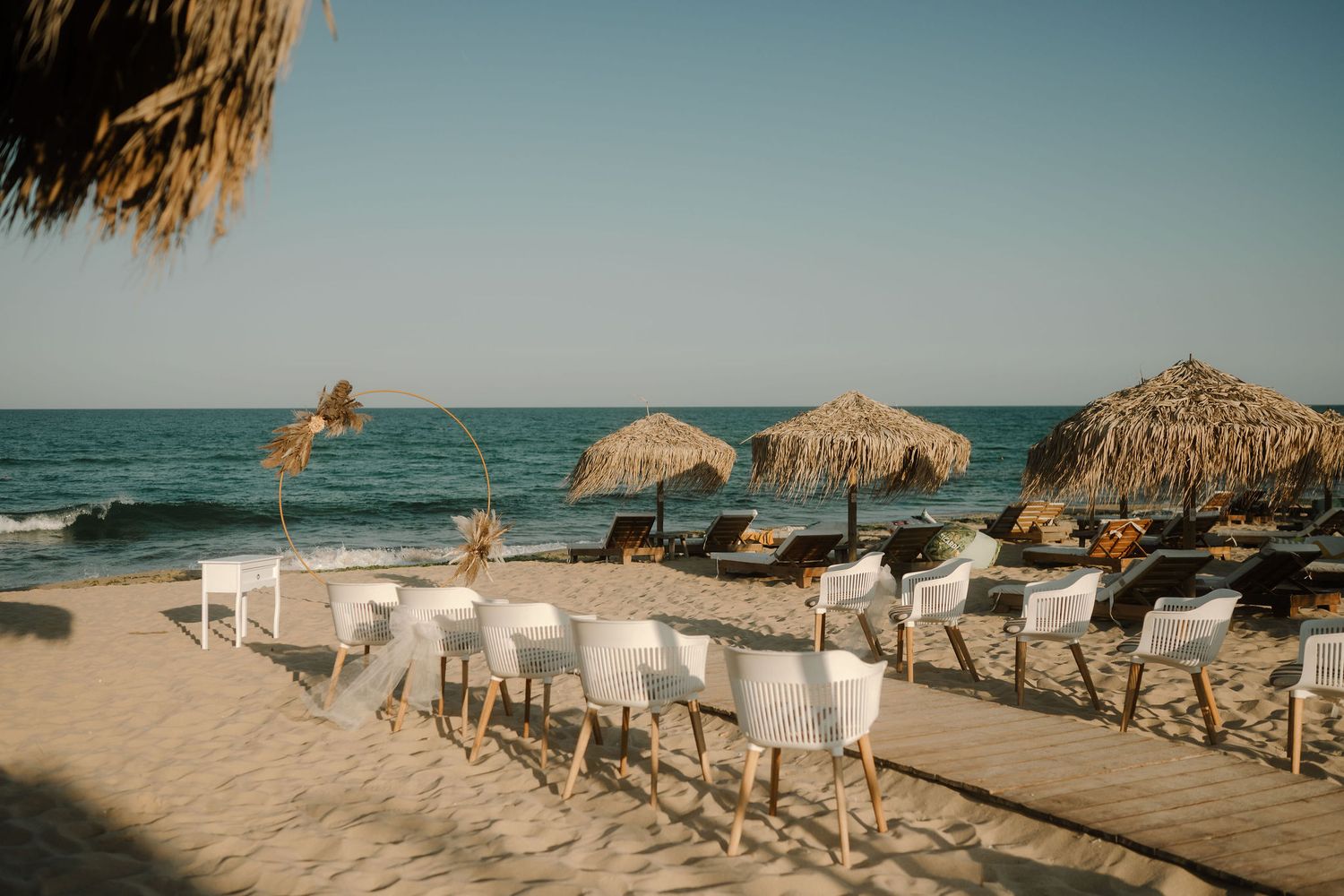 Beach chairs and thatched umbrellas line a sandy shoreline with turquoise ocean waters and warm sunlight.