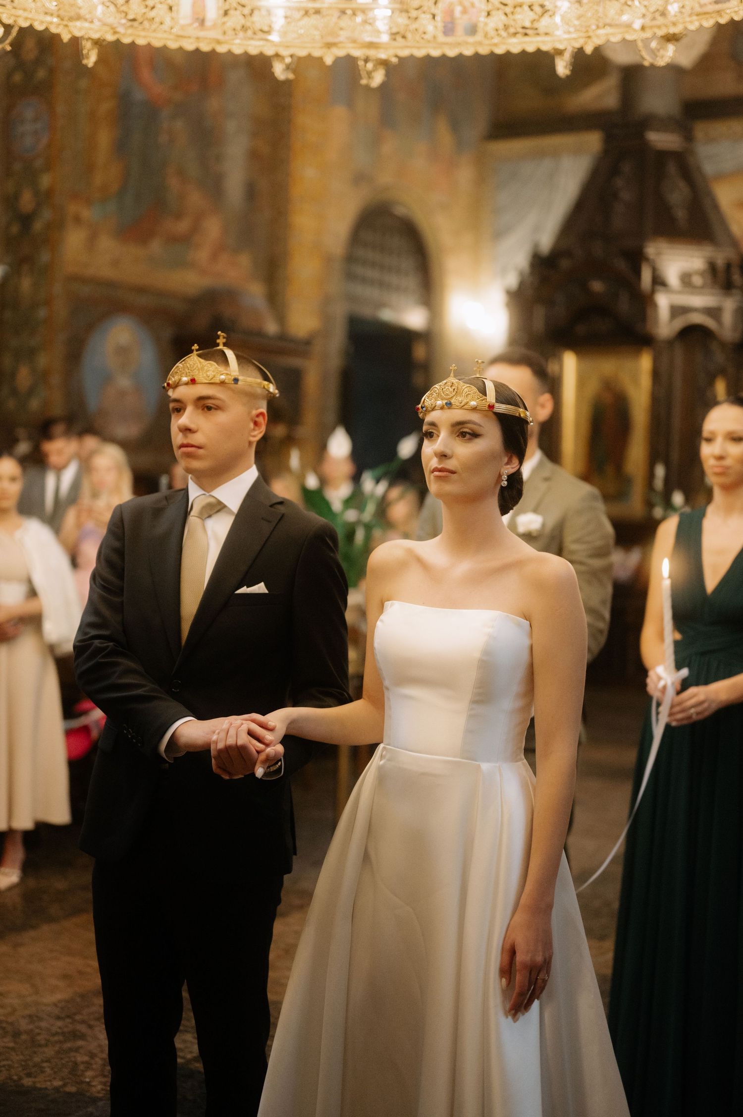 A formal wedding ceremony in an elegant ballroom with crystal chandeliers and guests in black tie attire.