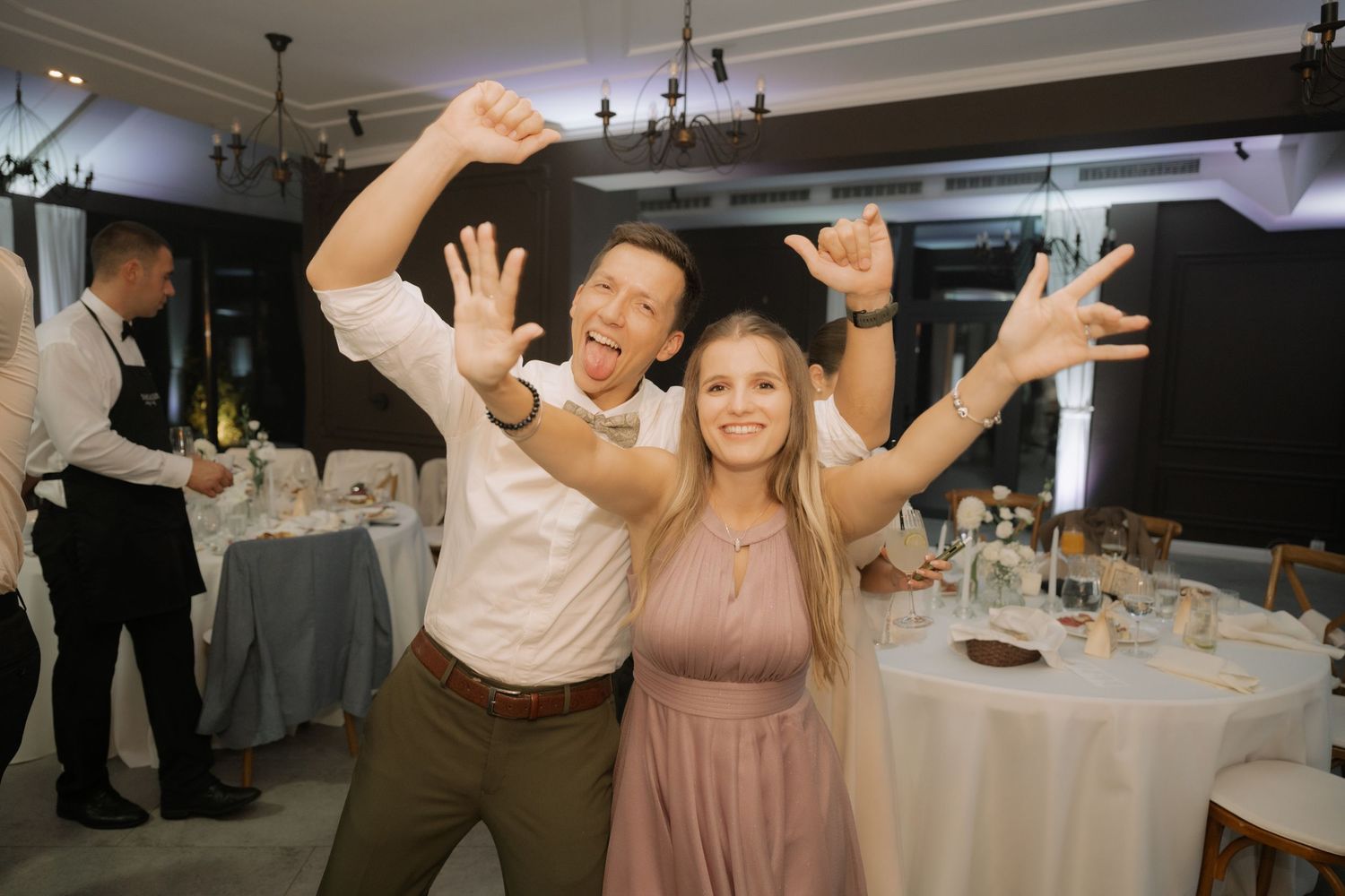 Wedding guests dance and celebrate on a crowded reception dance floor with raised arms and joyful expressions.