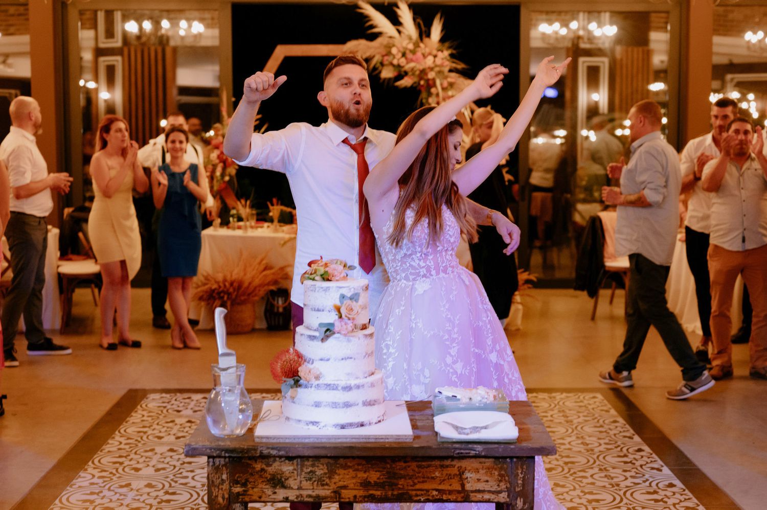 Wedding guests dance and celebrate on an illuminated dance floor during an elegant indoor reception.
