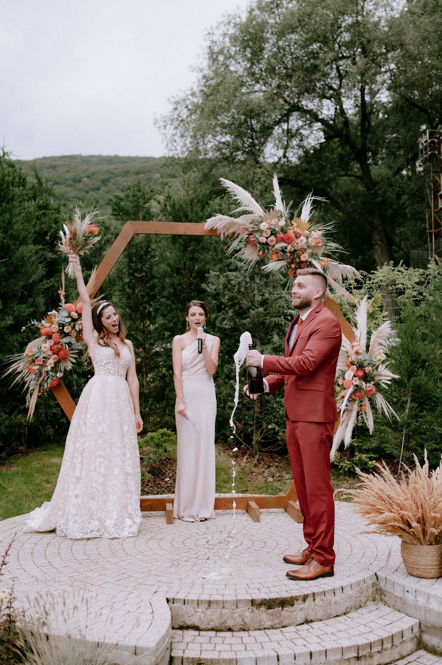 Wedding ceremony on a curved stone platform surrounded by lush greenery and decorated with dried floral arrangements.