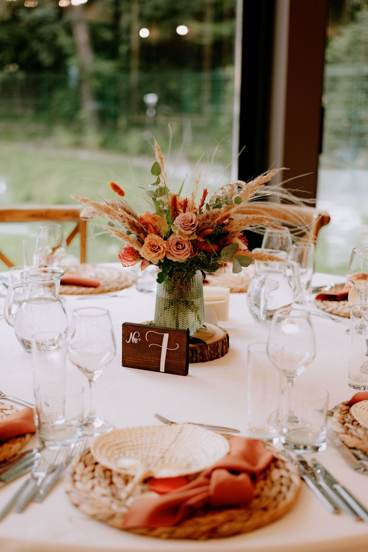 Elegant wedding reception table settings with rustic floral centerpieces, crystal glasses and coral napkins on white linens.
