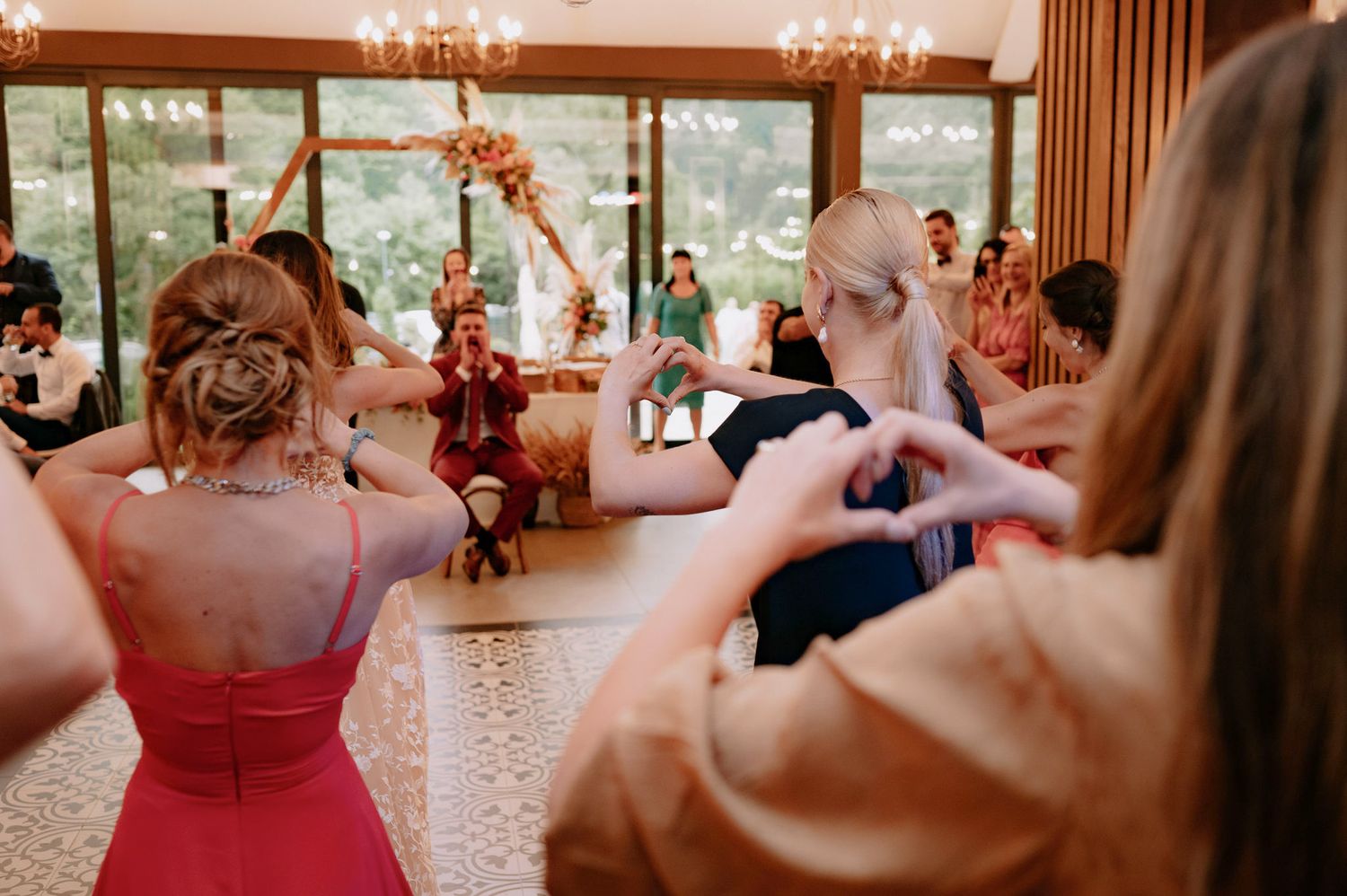 Wedding guests dance and celebrate on a wooden dance floor beneath elegant chandeliers at an evening reception.