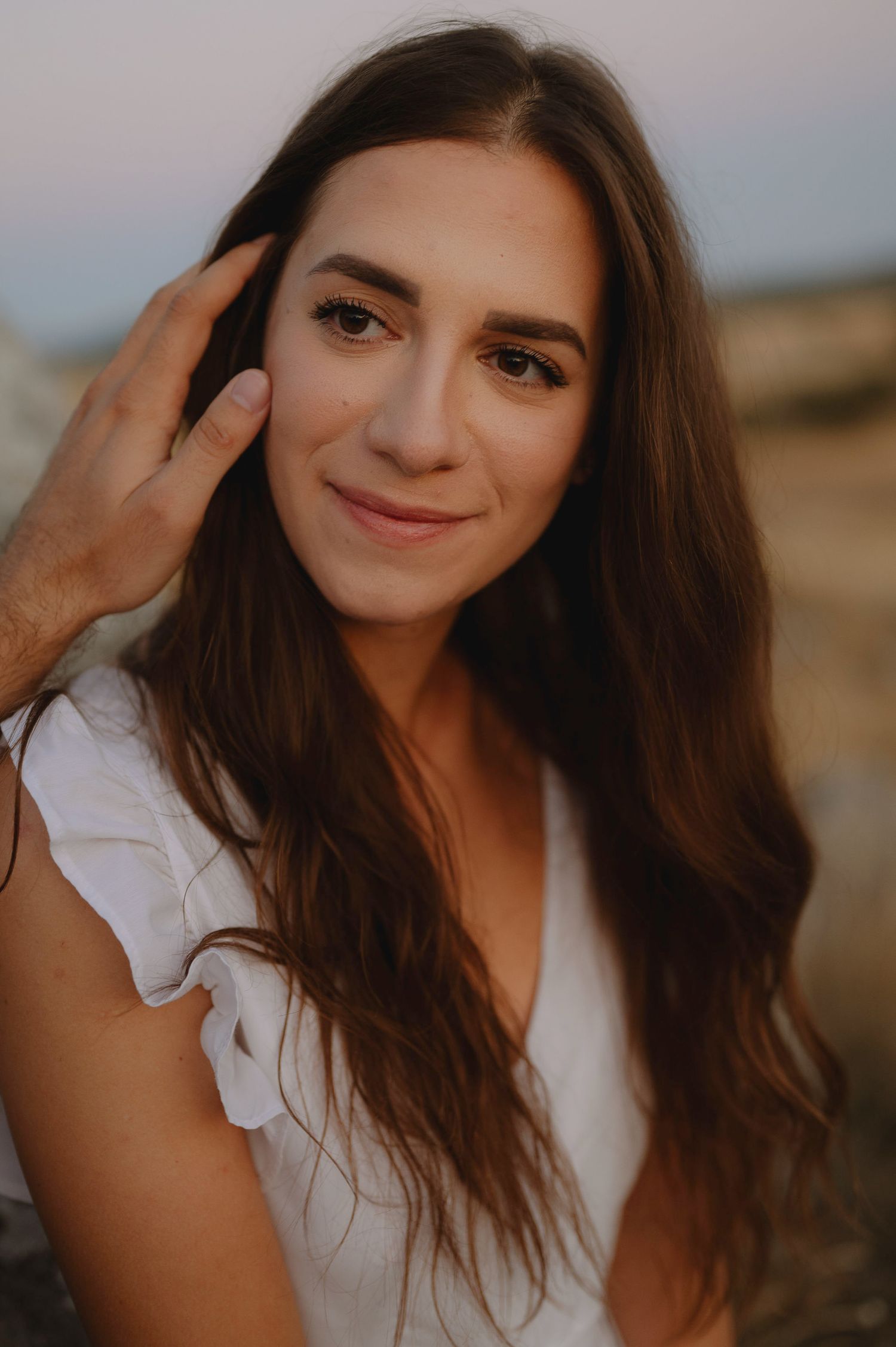 Close-up portrait shots of a woman with flowing brown hair in a white dress against a warm sunset backdrop.