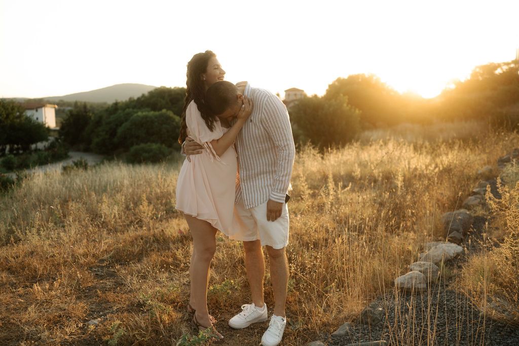Couple embraces in golden sunlit field during sunset engagement photoshoot.