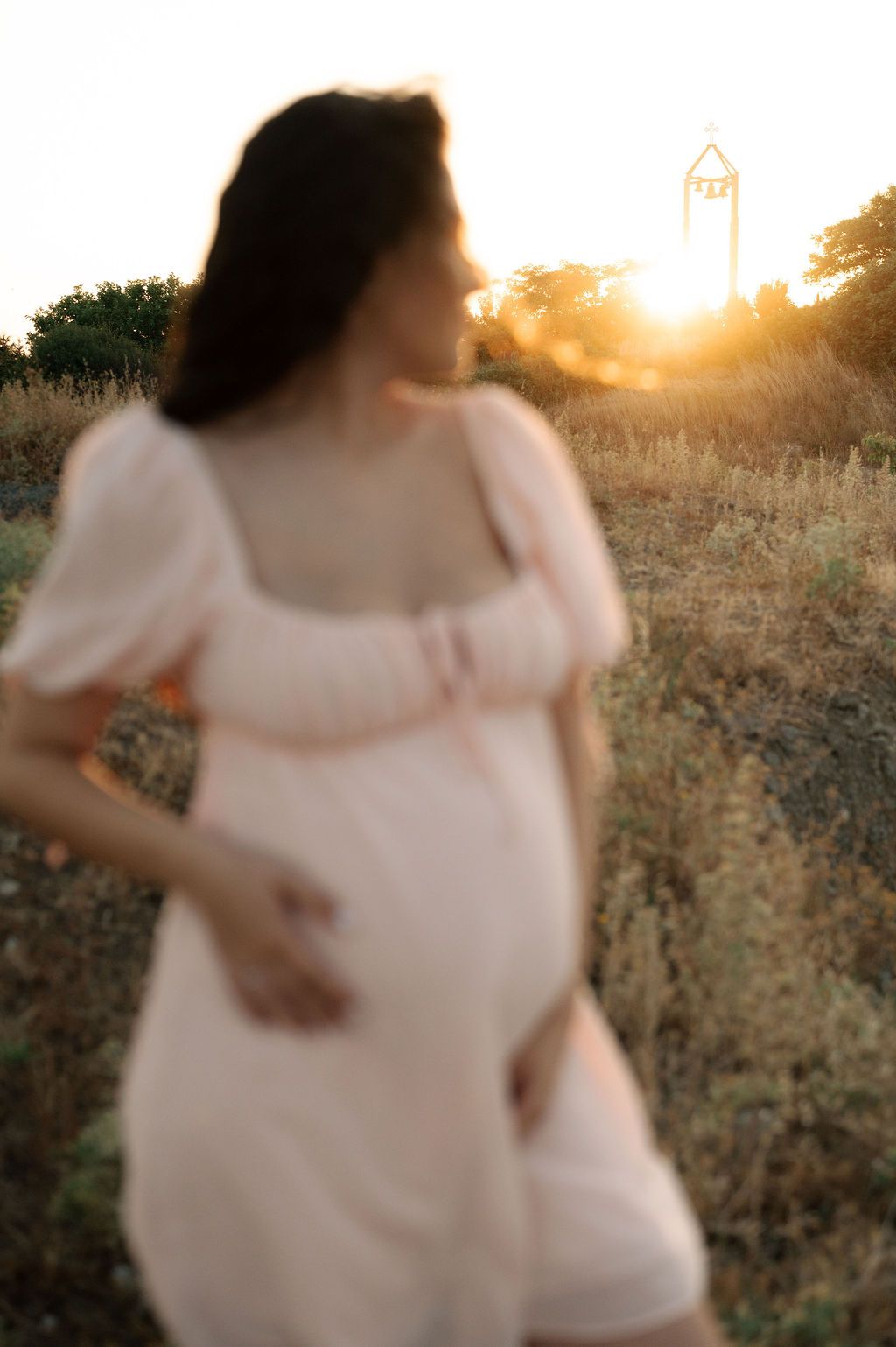 A figure in a flowy white dress spins gracefully in a golden sunlit field during sunset.