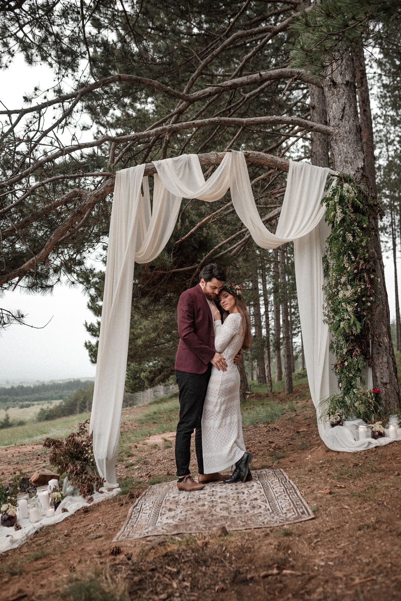 A romantic outdoor wedding scene with draped white curtains between trees in a rustic forest setting.