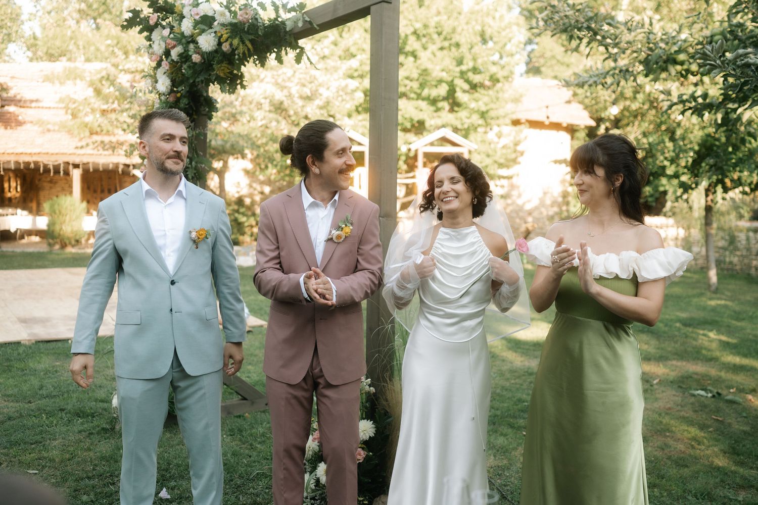 Wedding party members share a joyful moment walking together outdoors in pastel suits and dresses.
