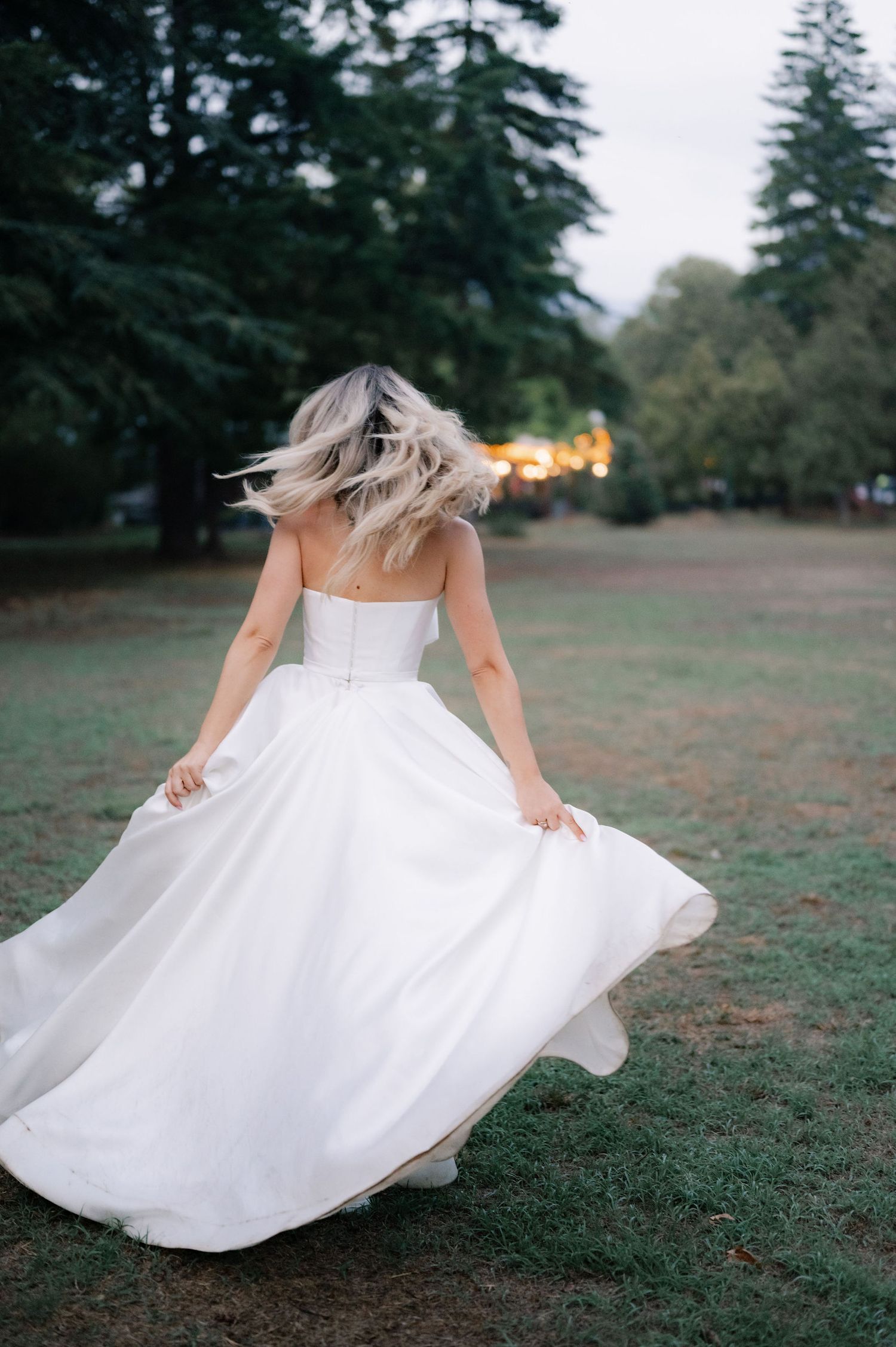 A person in a flowing white wedding dress twirls gracefully in a grassy field at sunset.