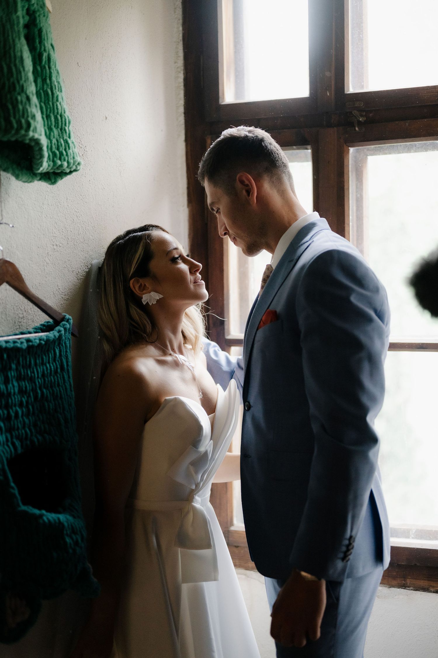 A couple in wedding attire share an intimate moment by a window in a series of romantic photos.