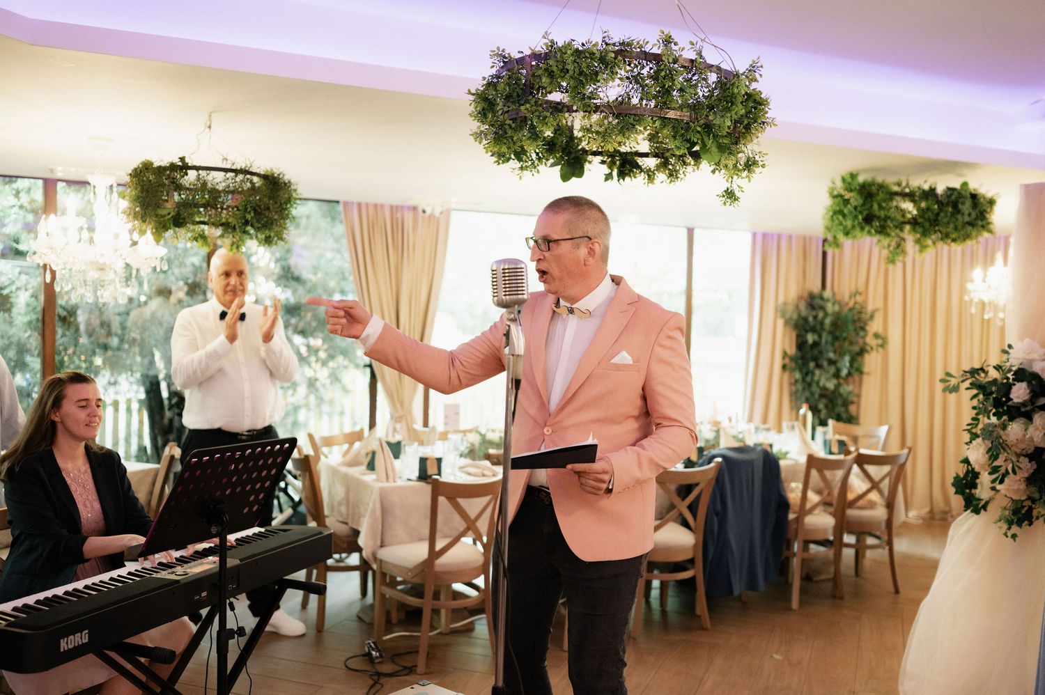 A pianist performs at an elegant indoor venue decorated with greenery and cross-back chairs for an event.