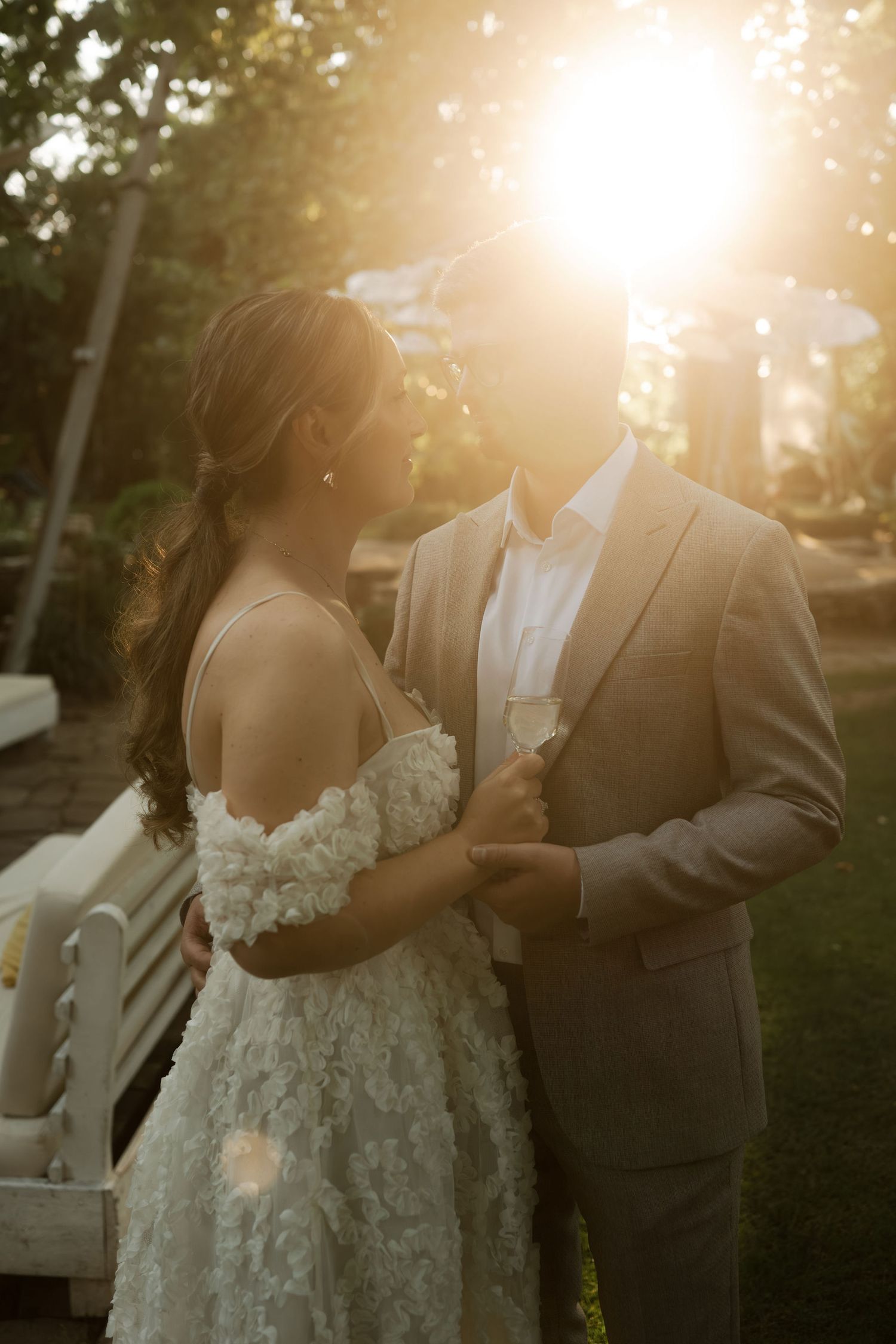 A couple shares an intimate moment in golden sunset light while wearing wedding attire in an outdoor setting.