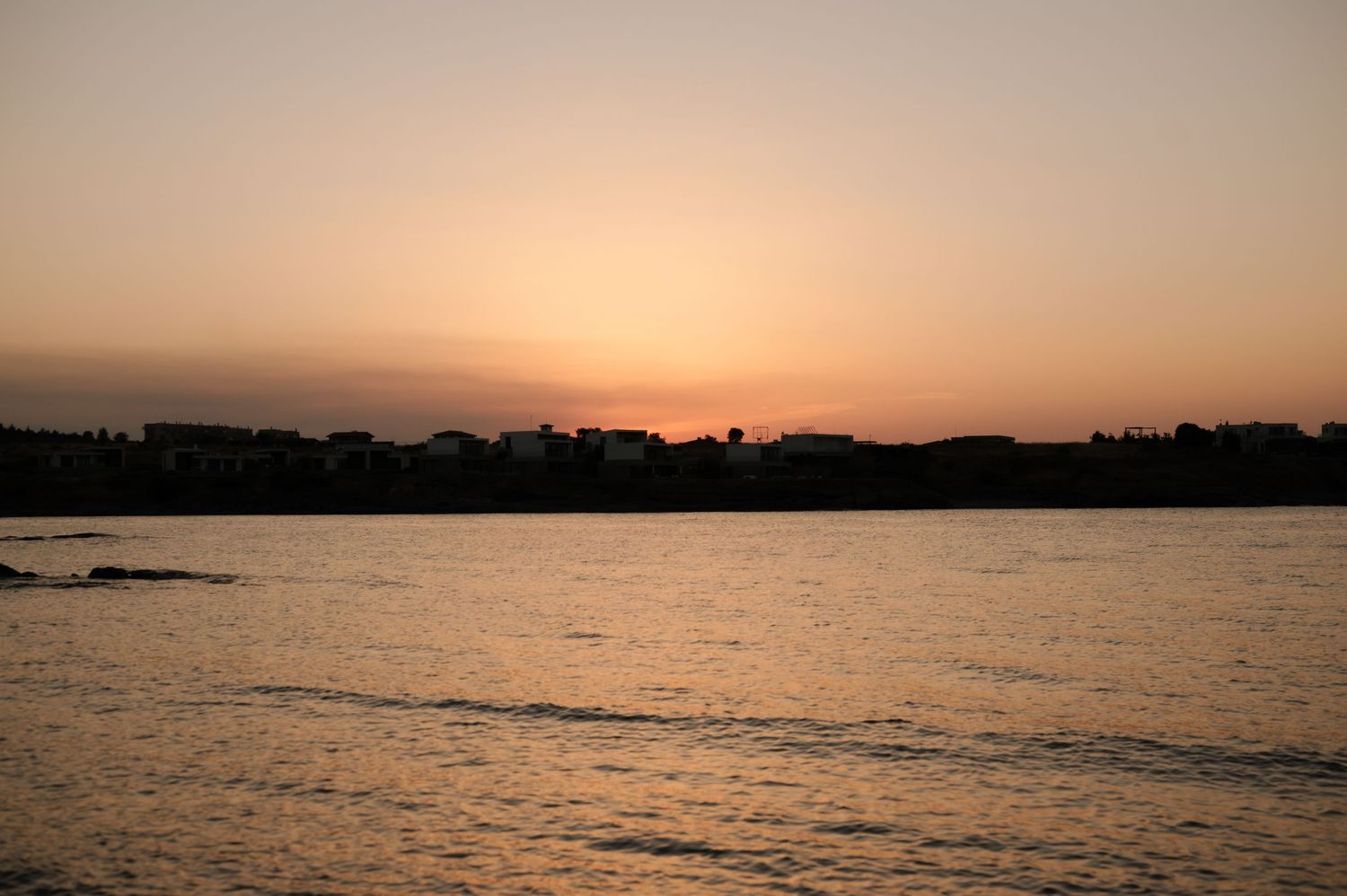 A panoramic view of a tranquil ocean at sunset with silhouetted buildings along the coastline.