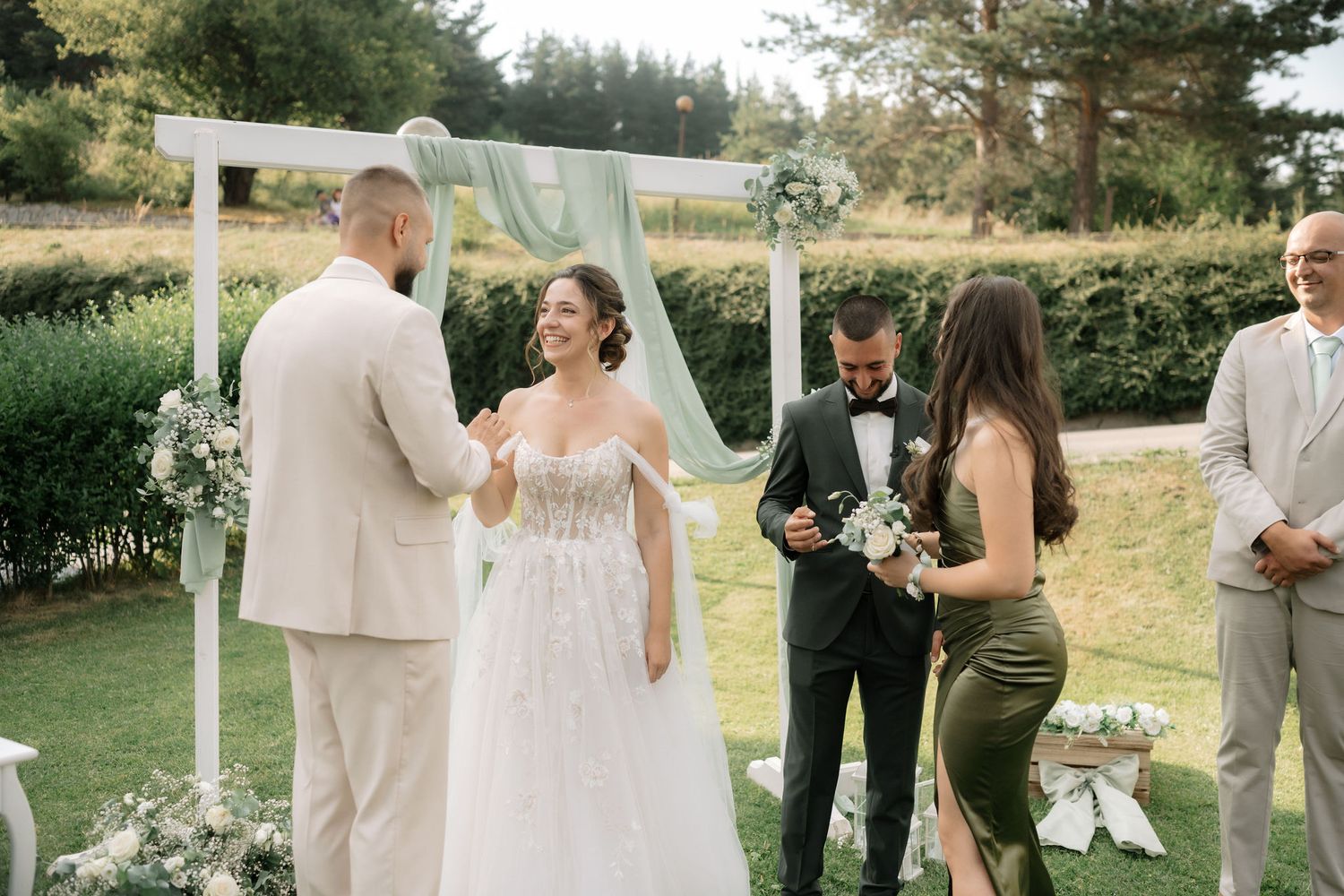 Wedding party in light beige and black attire poses outdoors during a summer garden ceremony celebration.